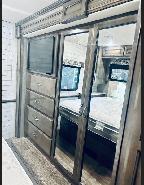 Comfortable RV rental bedroom with a mounted TV, dresser drawers, and full-length mirrored closet doors. Modern RV living!. Fleetwood Bounder 2018