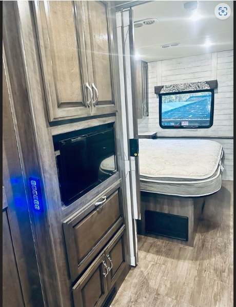 Experience this RV rental's cozy bedroom area, complete with built-in storage, TV, and a lit control panel, ideal for travel.. Fleetwood Bounder 2018