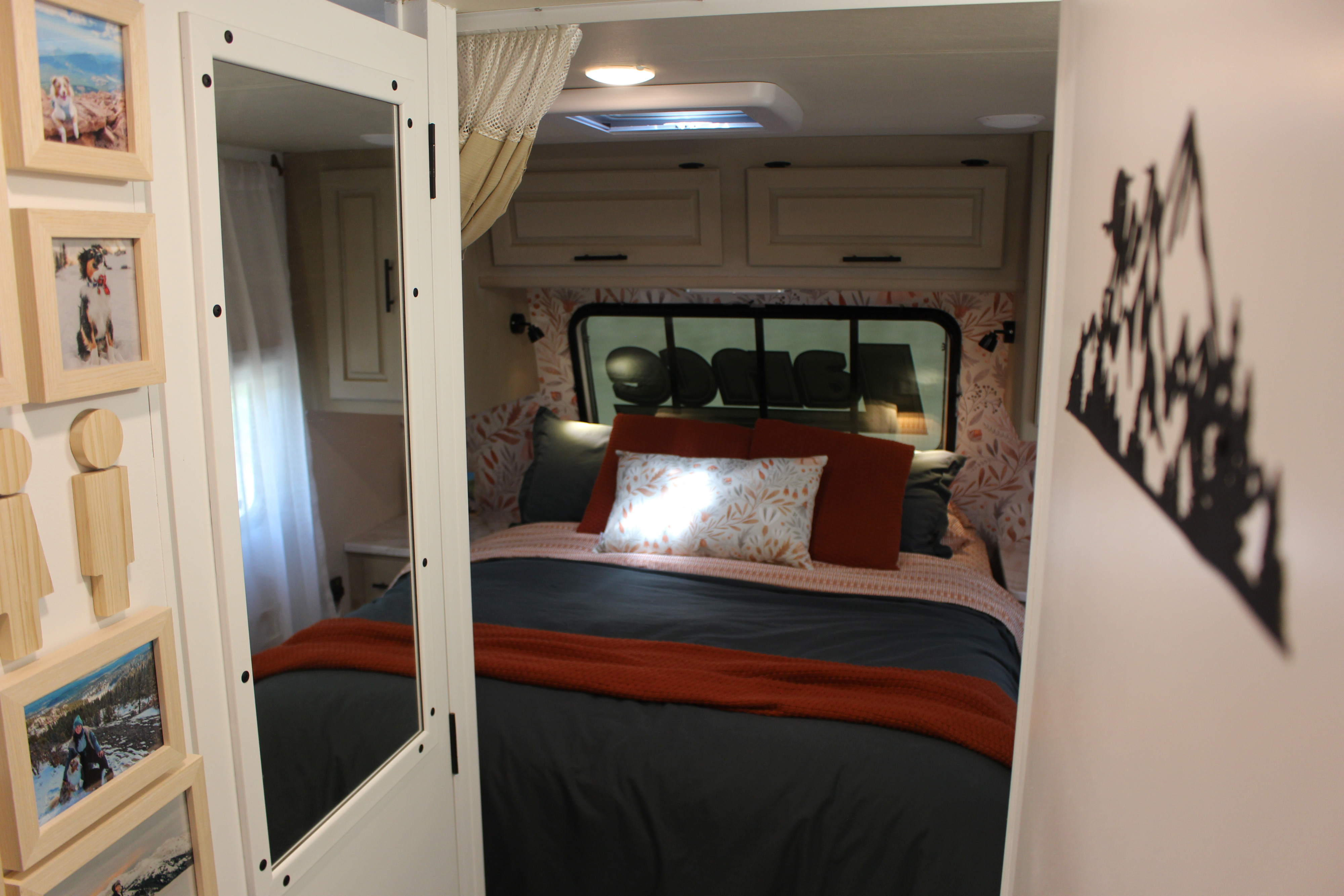 Comfortable RV rental bedroom with dark bedding, orange accents, patterned headboard, and overhead storage cabinets.. Lance Manufacturing Lance Manufacturing Trailer 2015