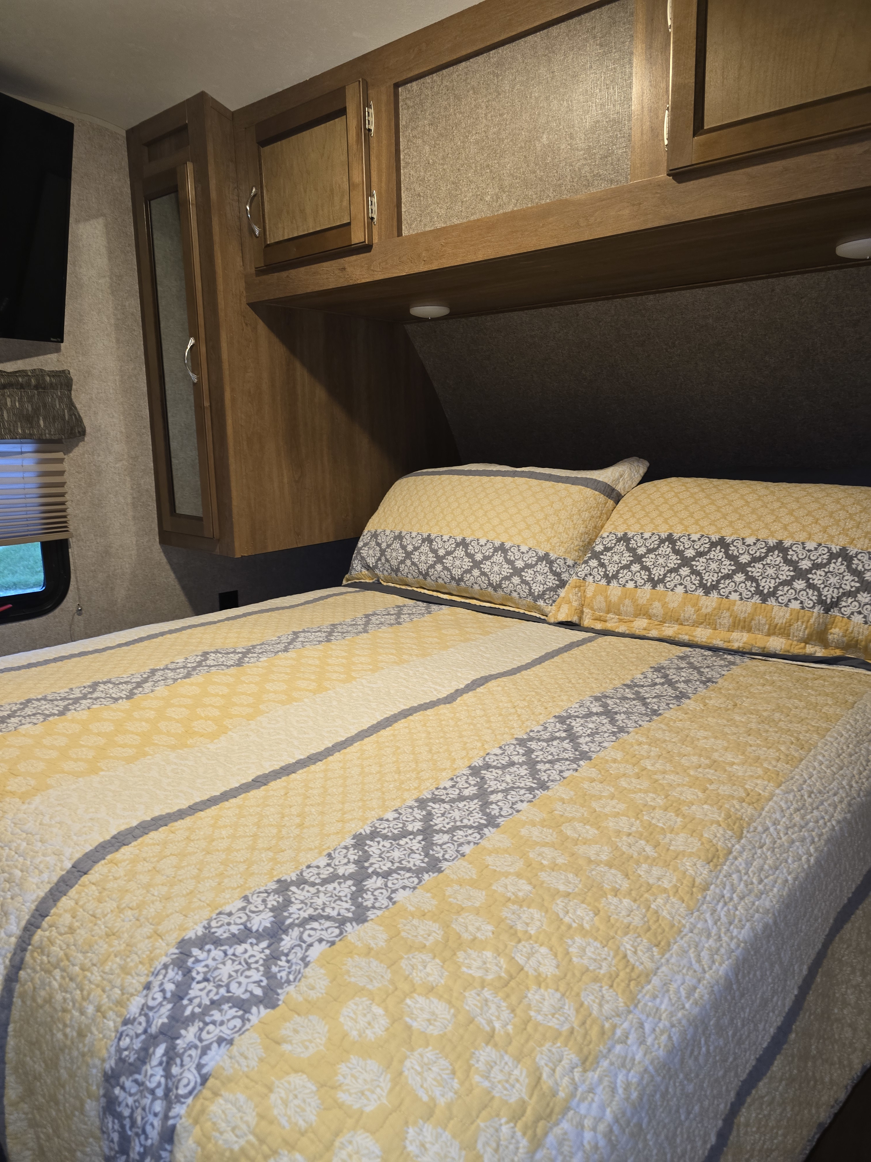 RV rental interior: A welcoming bedroom with a yellow and gray patterned quilt, pillows, and wooden cabinets.. Coachmen Catalina legacy 2017