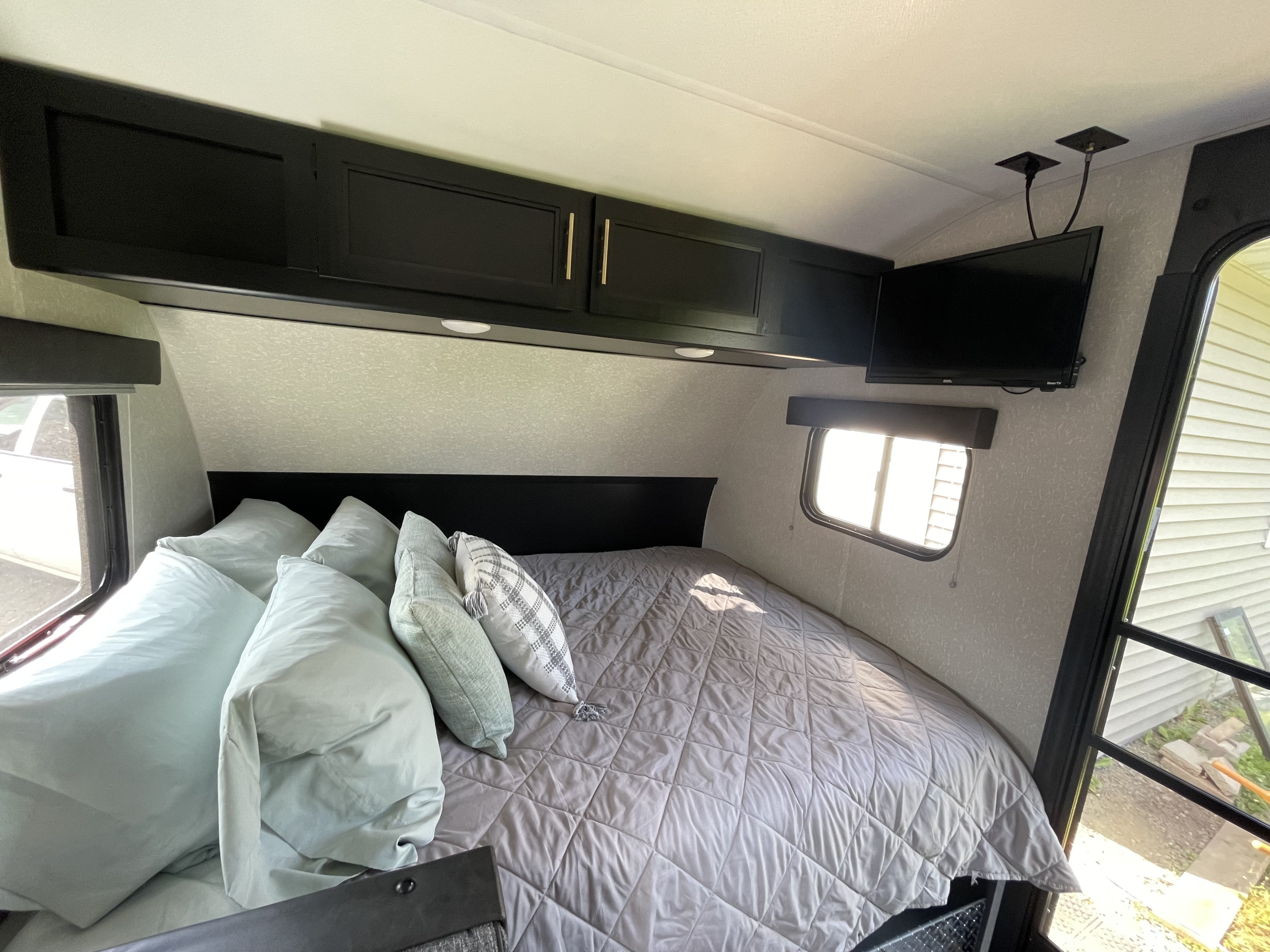 Inside an RV rental: cozy bedroom featuring a bed with pillows, black overhead cabinets, and a wall-mounted TV.. Forest River Cherokee Wolf Pup 2022