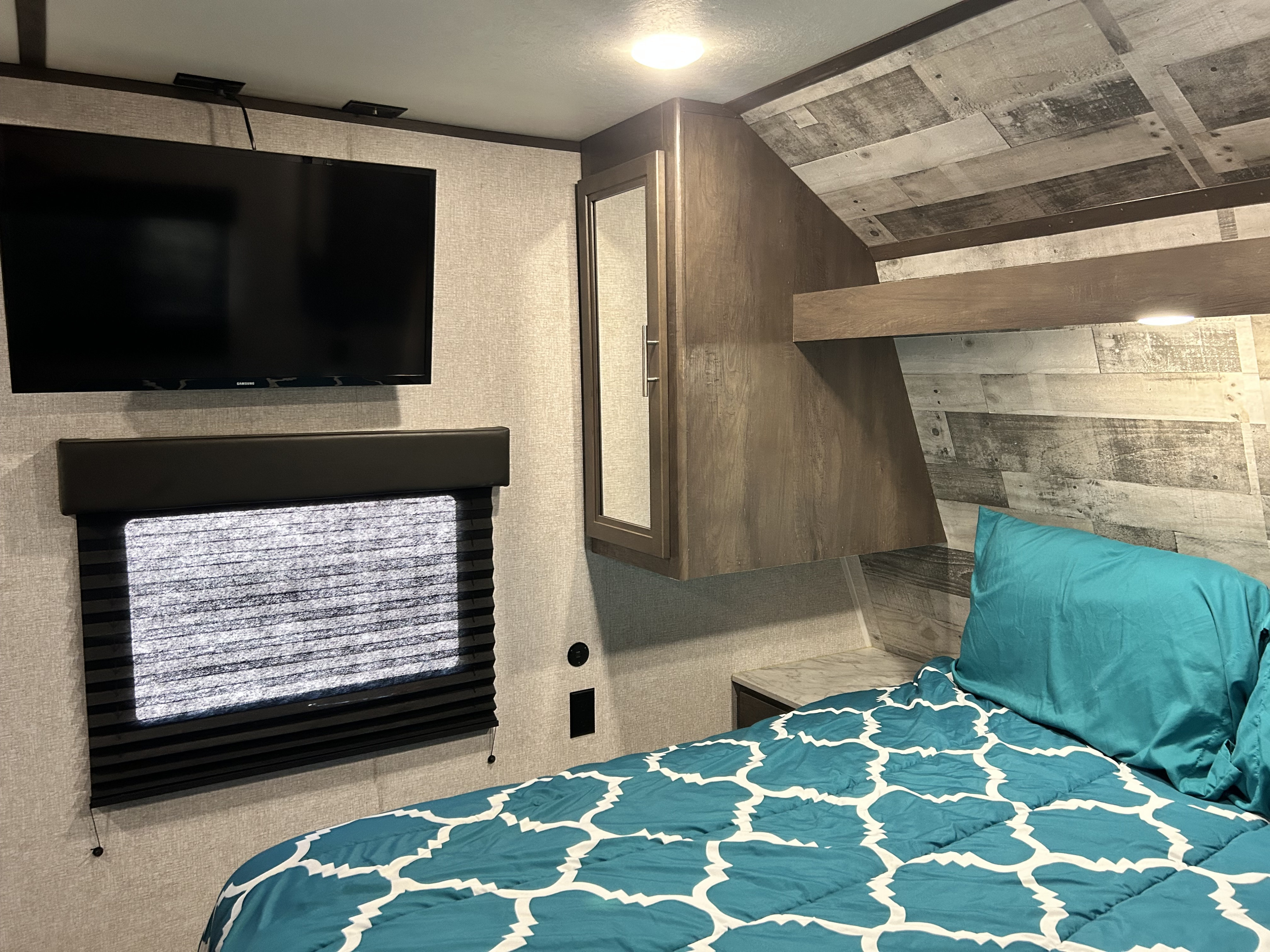 This RV rental bedroom offers comfort with a mounted TV, window blind, and stylish wood paneling for your travels.. Dutchmen Coleman Lantern 2021