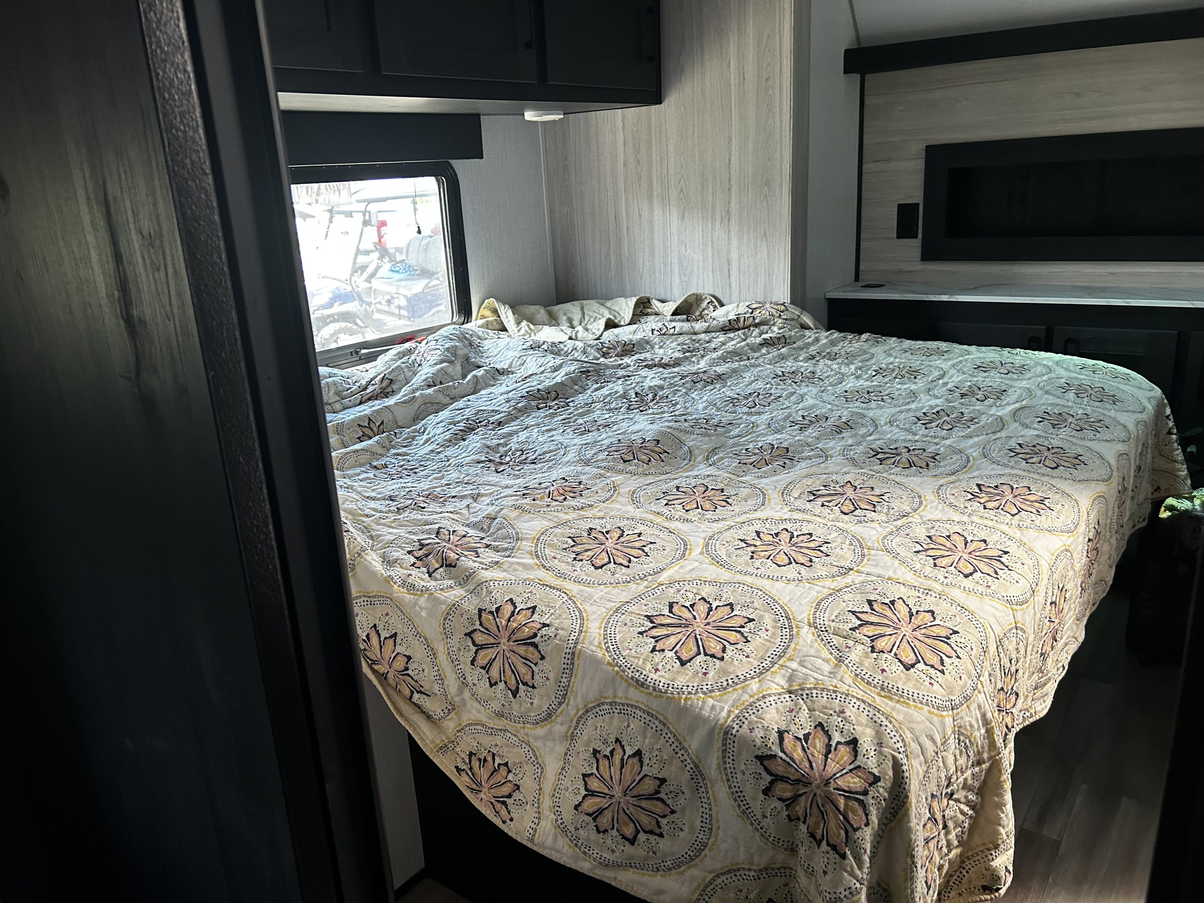 Spacious RV rental bedroom with a neatly made bed featuring a unique patterned quilt, window view, and built-in storage.. R V C Stryker 2022