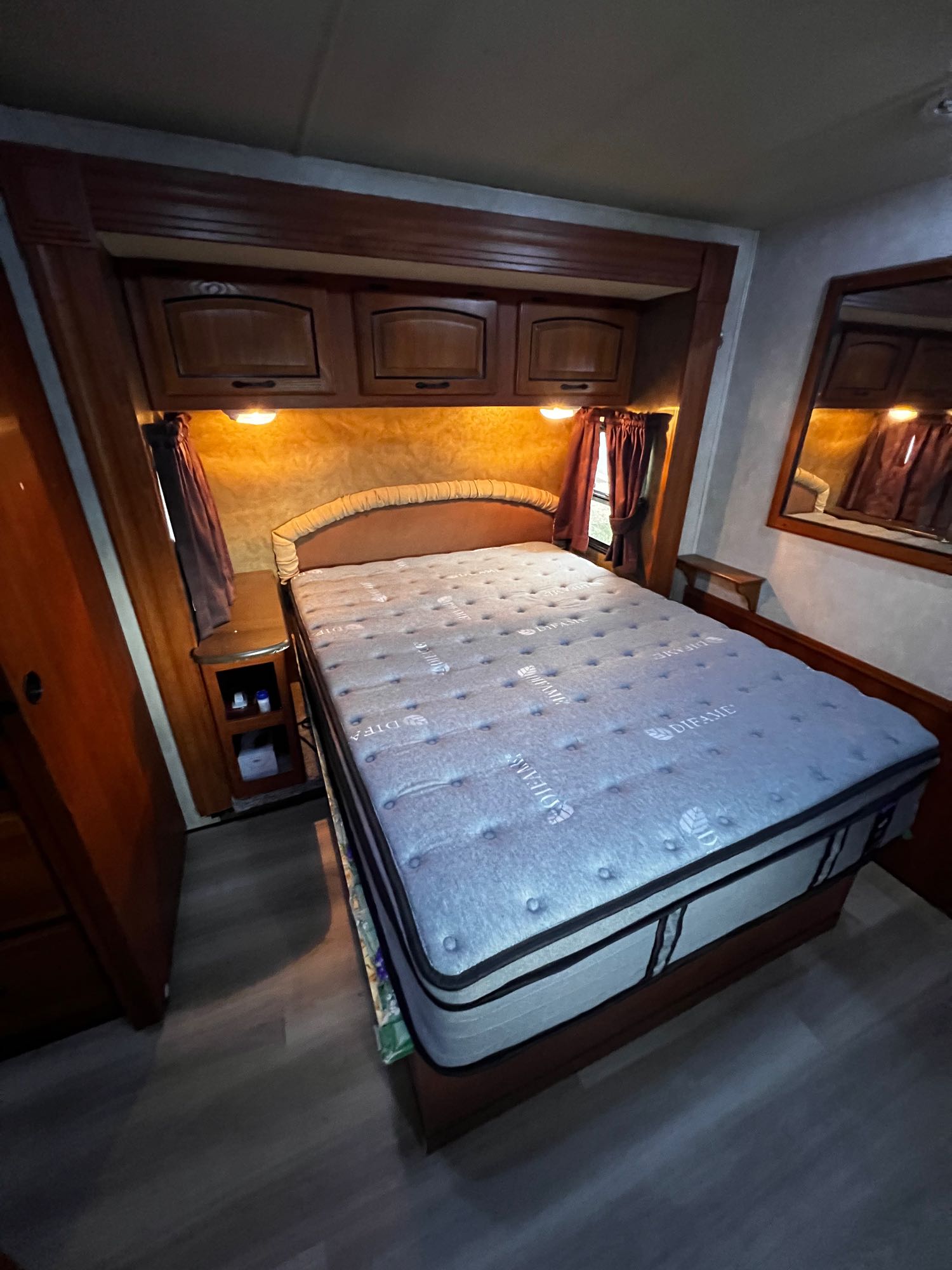 Cozy RV rental bedroom with a large mattress, overhead storage, and a bedside table, illuminated by warm lights.. Forest River Coachmen Mirada 32 DSF 2011