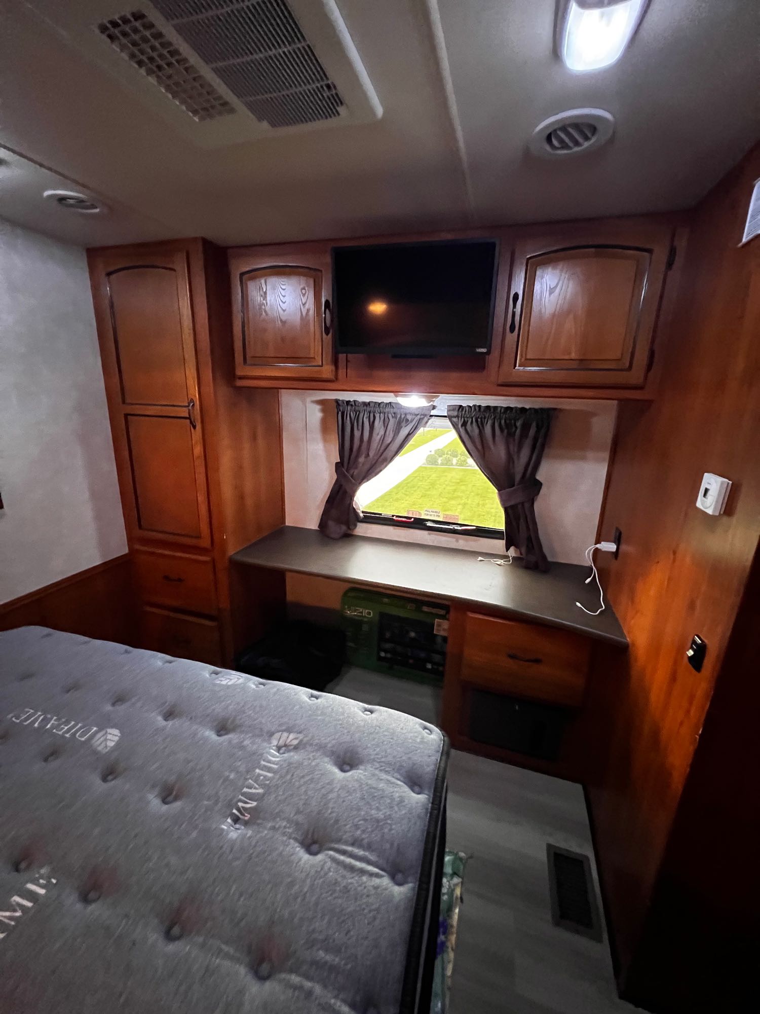 Compact RV rental bedroom featuring a comfy bed, TV, storage cabinets, and a window overlooking a green field.. Forest River Coachmen Mirada 32 DSF 2011