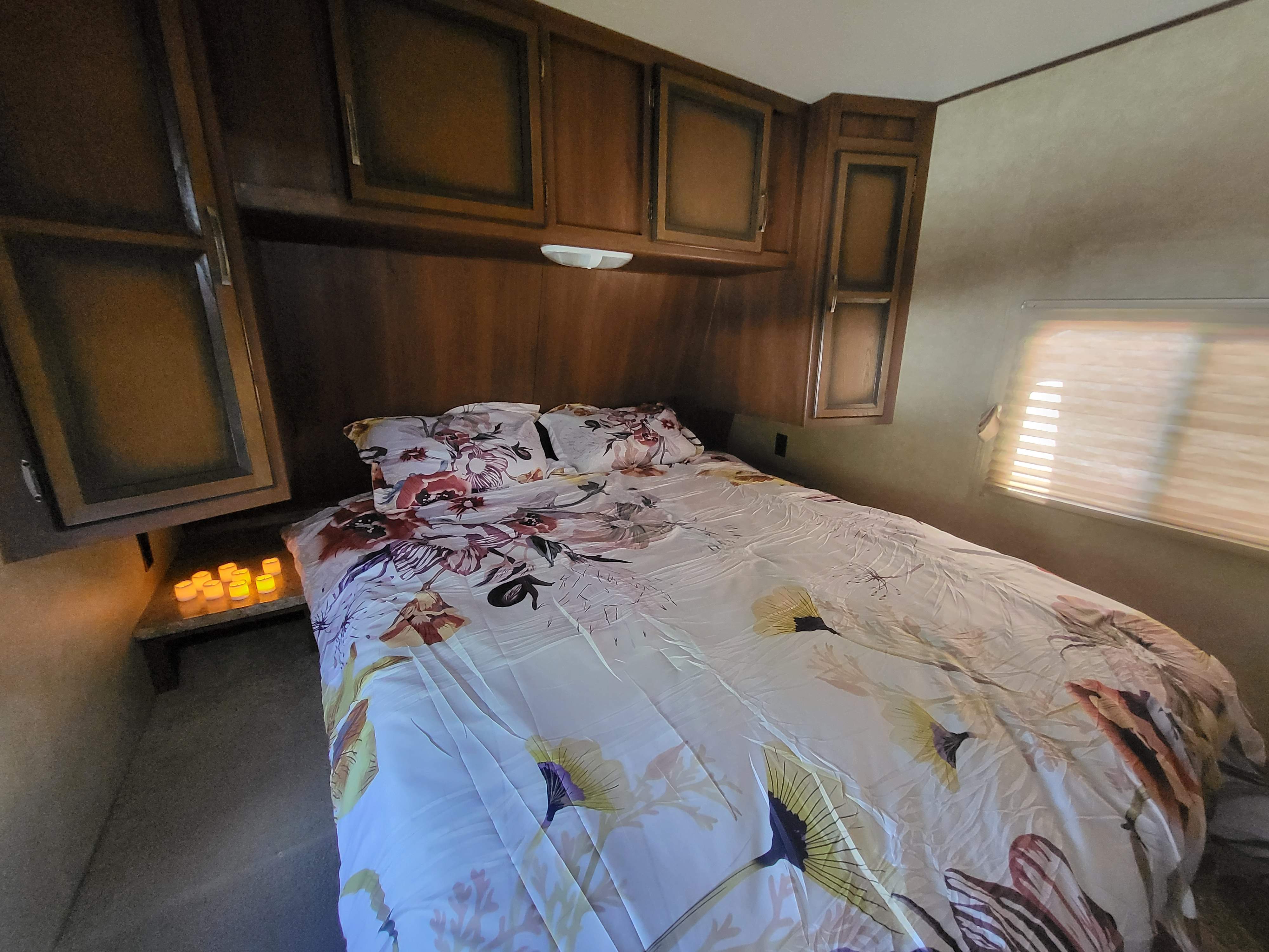 Cozy RV rental bedroom with floral duvet, overhead cabinets, and soft lighting for a comfortable stay.. Crossroads RV Longhorn 2014