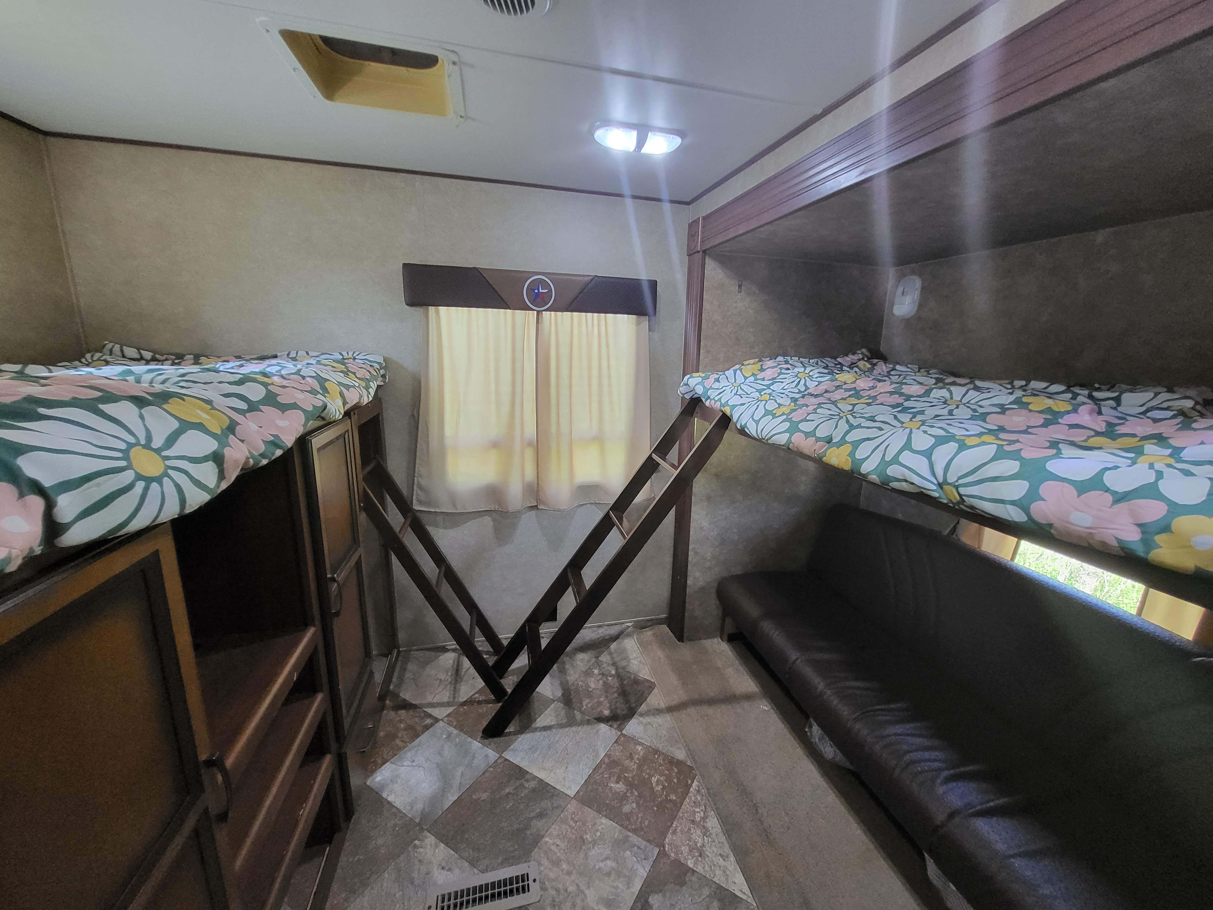 RV rental bunkhouse interior: Two floral bunk beds, one with ladder access, a convertible sofa, and built-in storage.. Crossroads RV Longhorn 2014