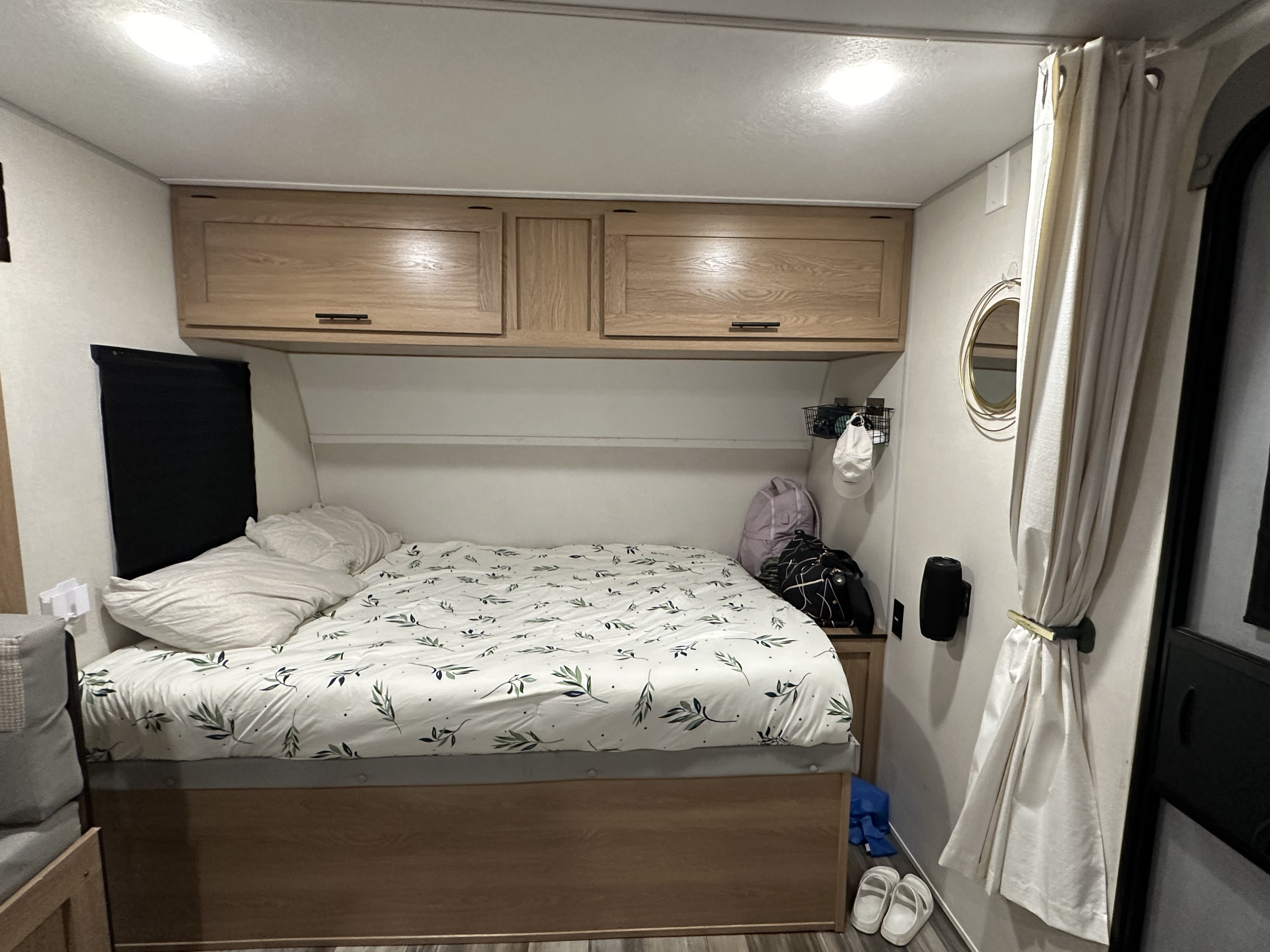 Inside a cozy RV rental bedroom: bed with leafy bedding, wood cabinets, and compact storage solutions.. Prime Time Avenger - 17BHS 2022