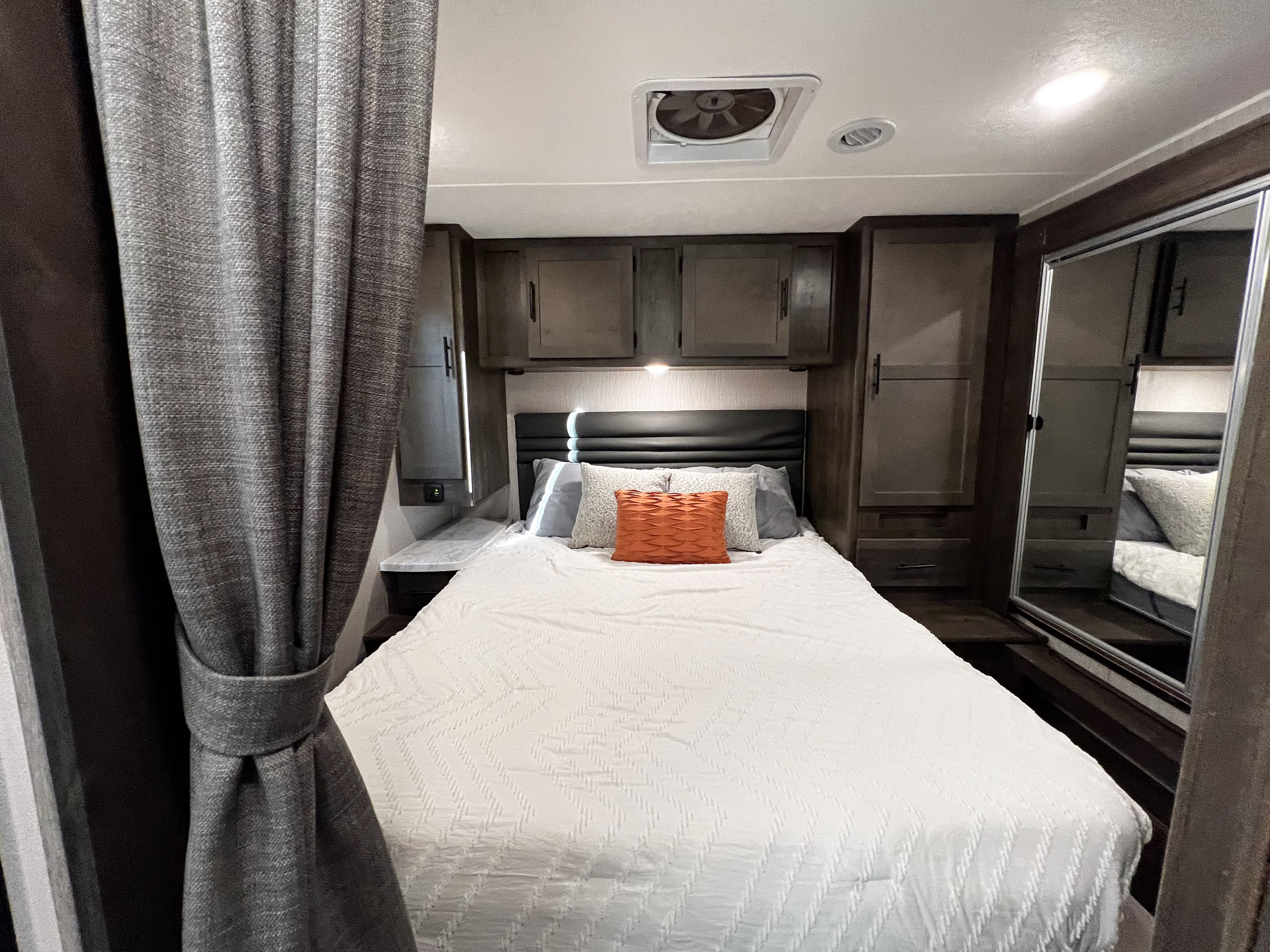 Cozy RV rental bedroom featuring a white bed, dark wood cabinets, and a ceiling fan, offering comfortable travel accommodations.. Coachmen Leprechaun 2022