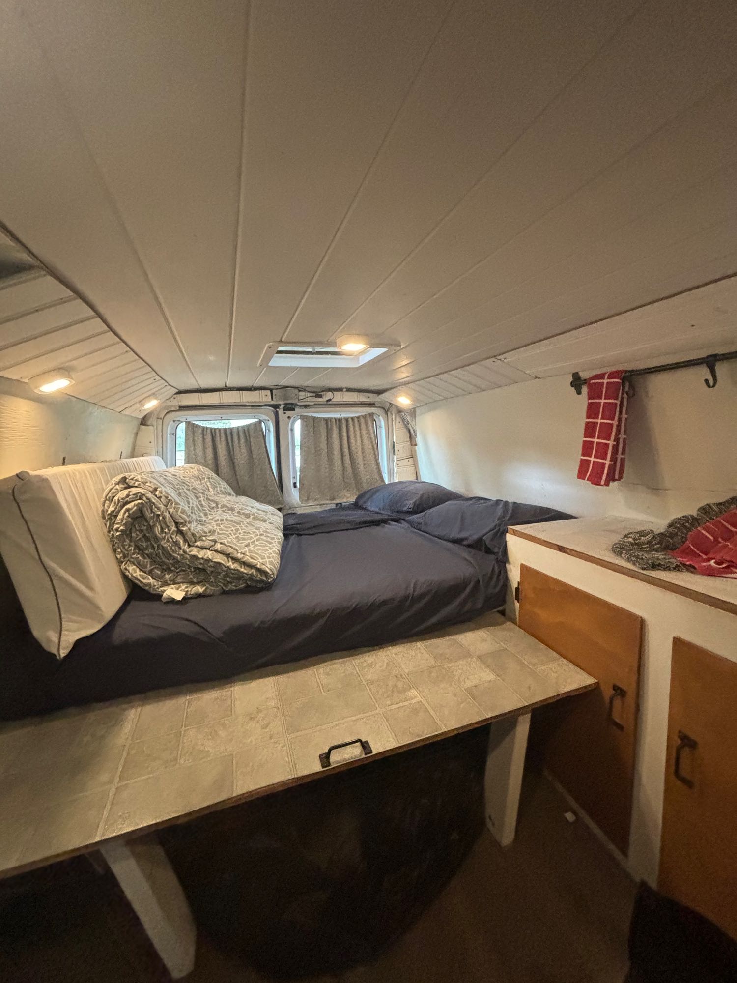 Cozy RV rental interior with a comfortable bed, window curtains, and built-in storage for mobile living.. Ford E250 Eagle Camper 2007