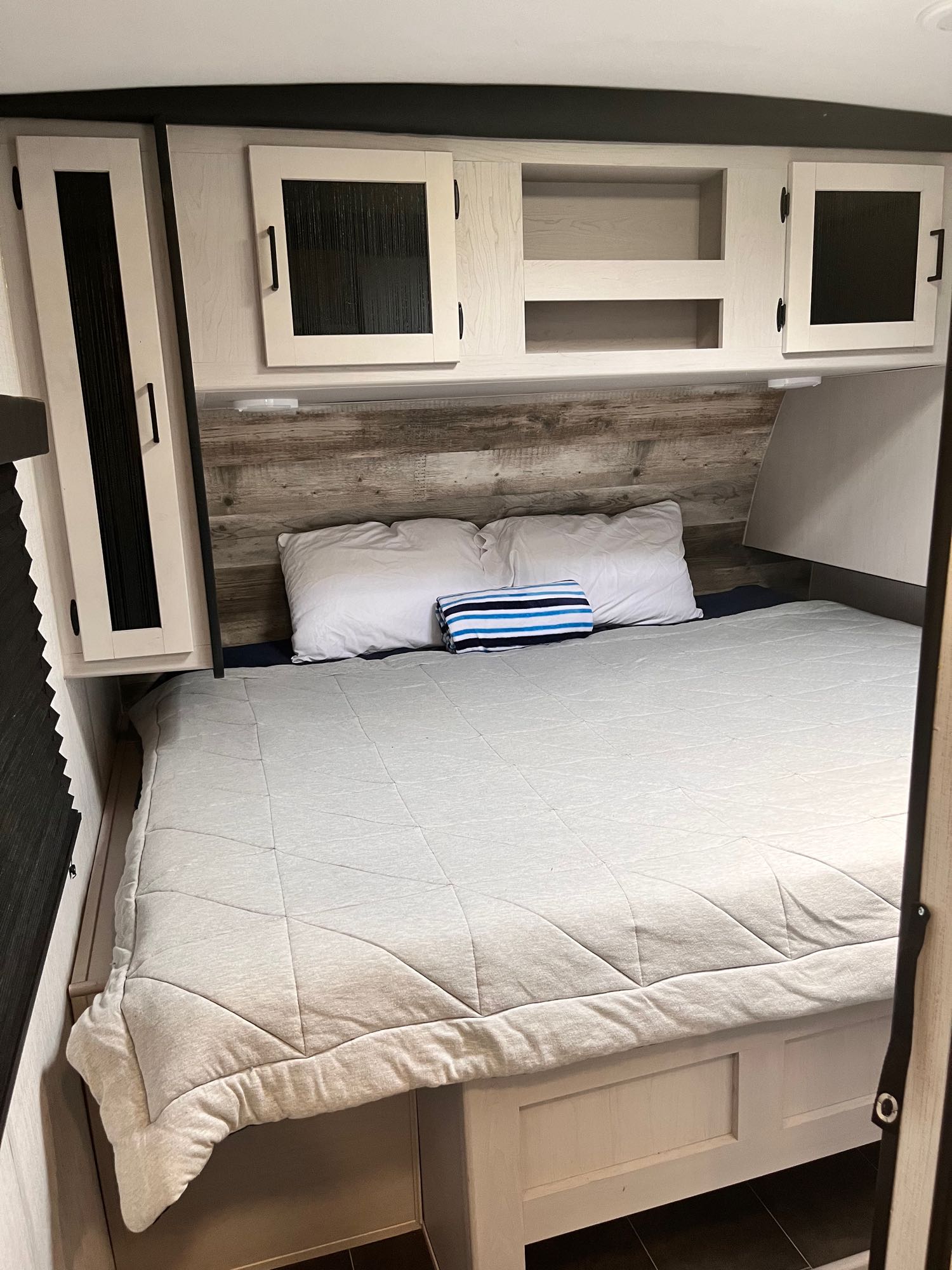 Inside an RV rental: a modern bedroom with a comfortable bed, rustic wood headboard, and light overhead storage cabinets.. Mallard Heartland 2022