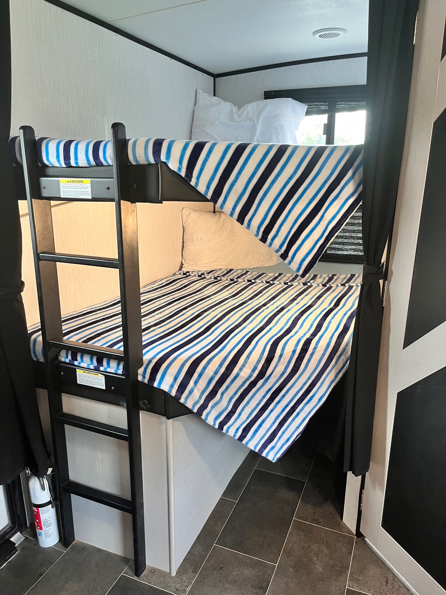 Inside an RV rental: a set of two bunk beds with blue and white striped blankets, a ladder, and safety equipment visible.. Mallard Heartland 2022