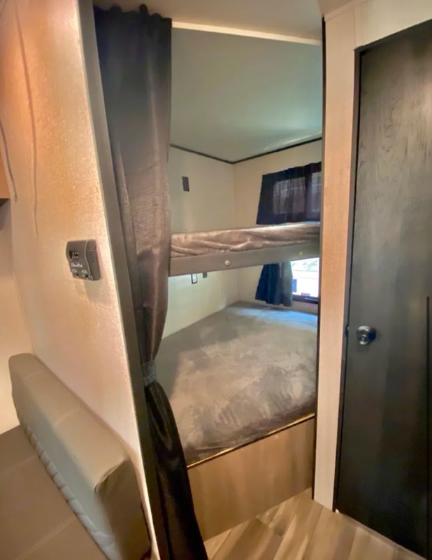 Cozy RV rental interior featuring a two-level bunk bed with grey bedding, a side sofa, and door. Perfect for families.. Starcraft Autumn Ridge 2022