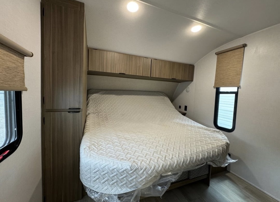 Cozy RV rental bedroom features a bed with overhead storage, a wardrobe, and windows with blinds for comfortable travels.. 4x4twdb22s7379119 Wildwood x lite 26 ice 2025