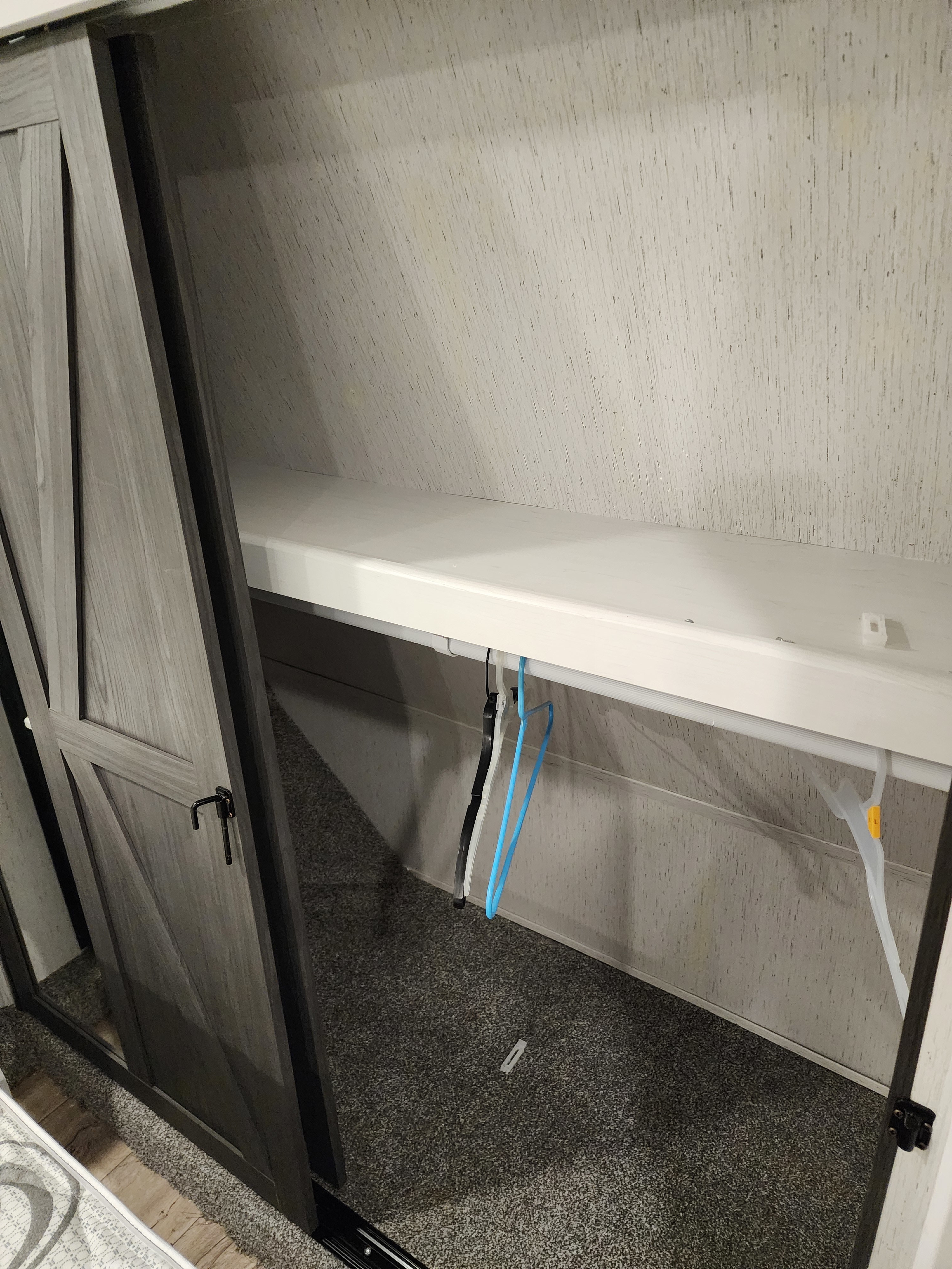 RV rental closet with a shelf, hanging rod, and empty hangers inside, behind a partially open sliding barn door.. Keystone RV AA3603LFP22 2022