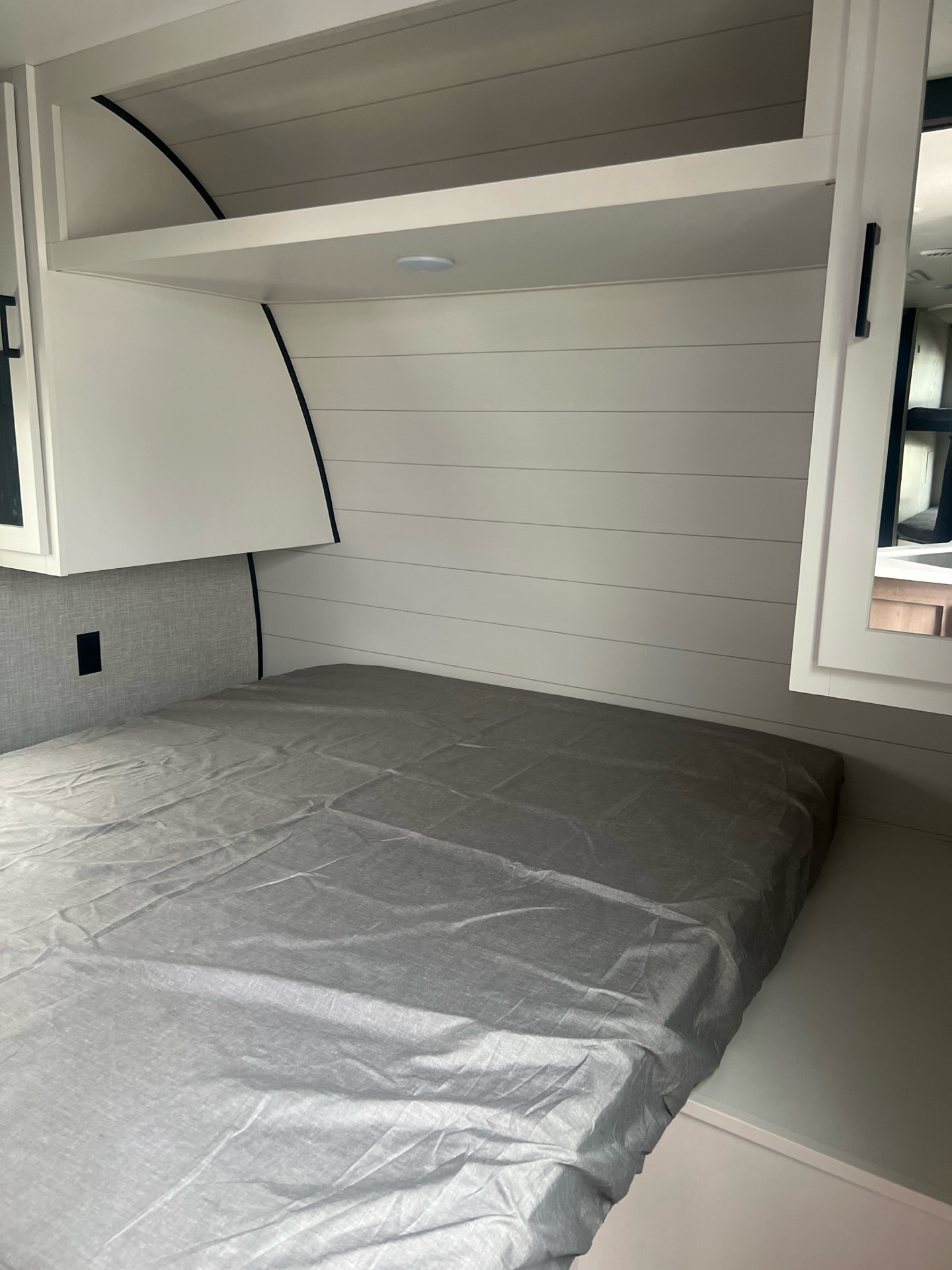 Compact RV rental bedroom featuring a gray bed, overhead cabinets, and stylish shiplap walls, ideal for comfortable sleep.. Starcraft Autumn Ridge 2024
