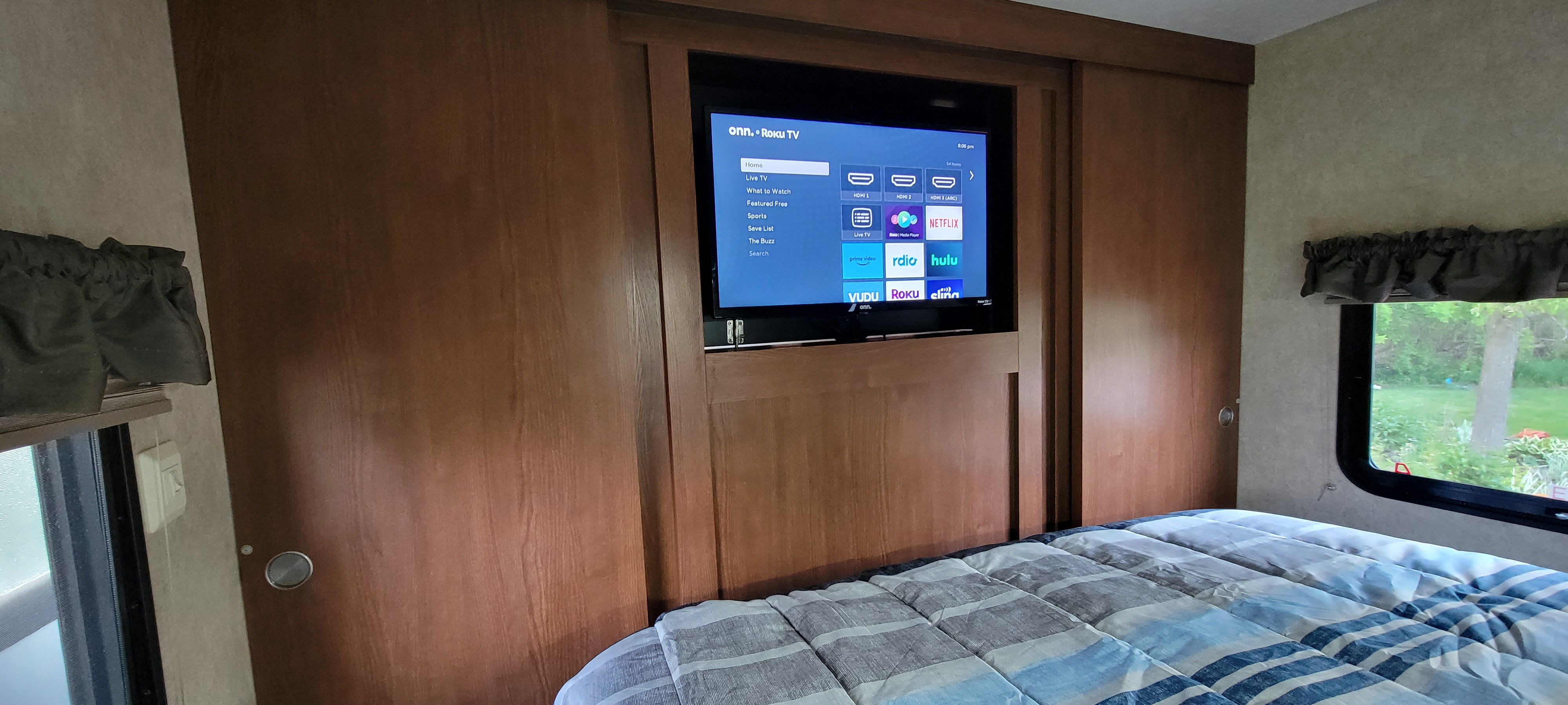 RV rental bedroom showing a built-in Roku TV with streaming apps over a comfortable bed.. Forest River Wildwood 2014