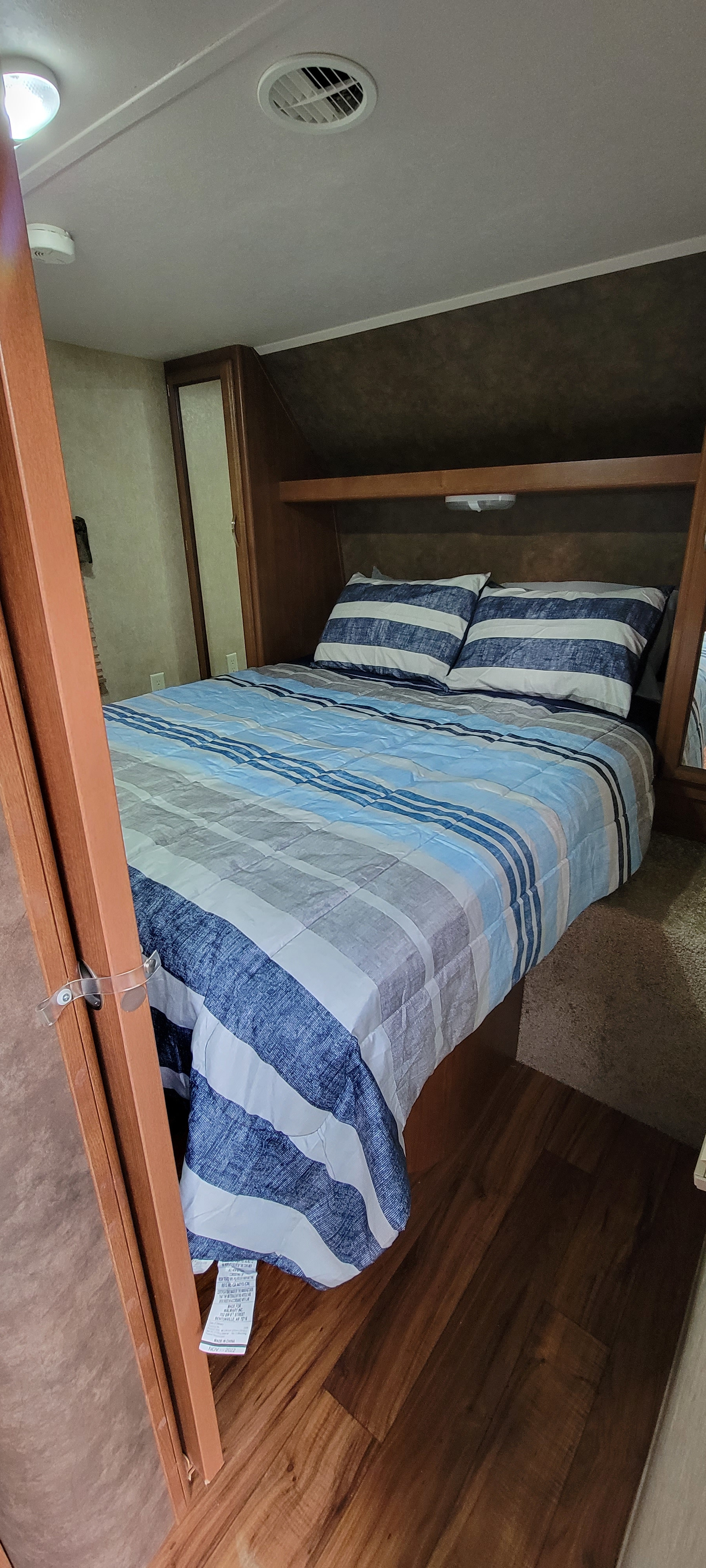 This cozy RV rental bedroom features a striped bed, wooden interior, and ceiling vent for comfort.. Forest River Wildwood 2014
