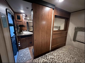 This RV rental interior features a wooden sliding door separating the kitchen area (left) from a cozy bedroom (right).. Jayco Jay Flight 2016