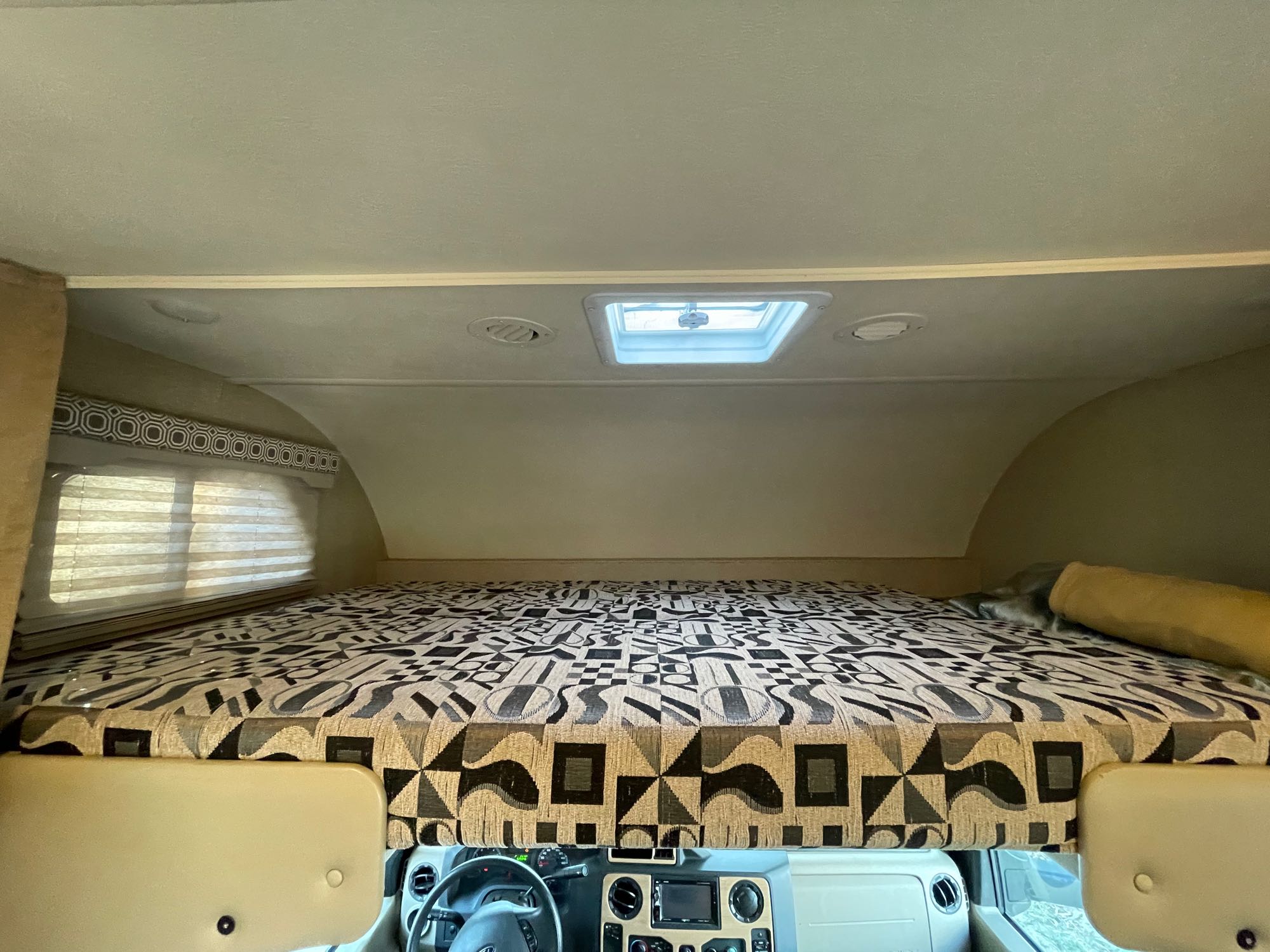 Inside an RV rental, featuring the spacious cab-over bunk with a patterned bed, skylight, and dashboard visible.. Thor Four Winds 2020