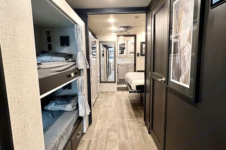 Explore this **RV rental** interior: bunk beds on left, leading down a hallway to a master bedroom & kitchen area.. Thor Motor Coach Tuscany 2023