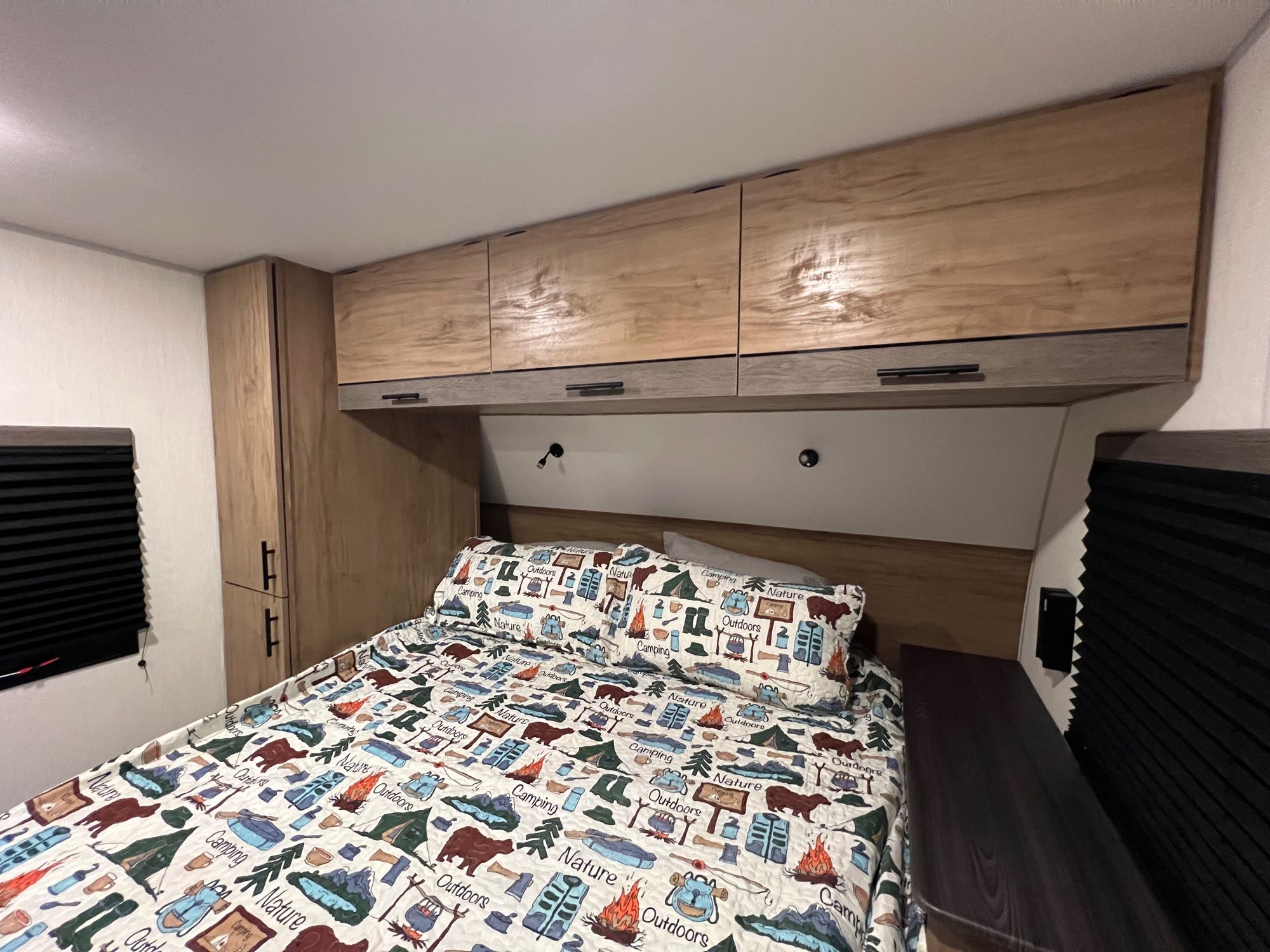 Cozy RV rental bedroom featuring nature-themed bedding, overhead storage, and black-out blinds for comfortable rest.. Forest River Campsite Reserve 2025