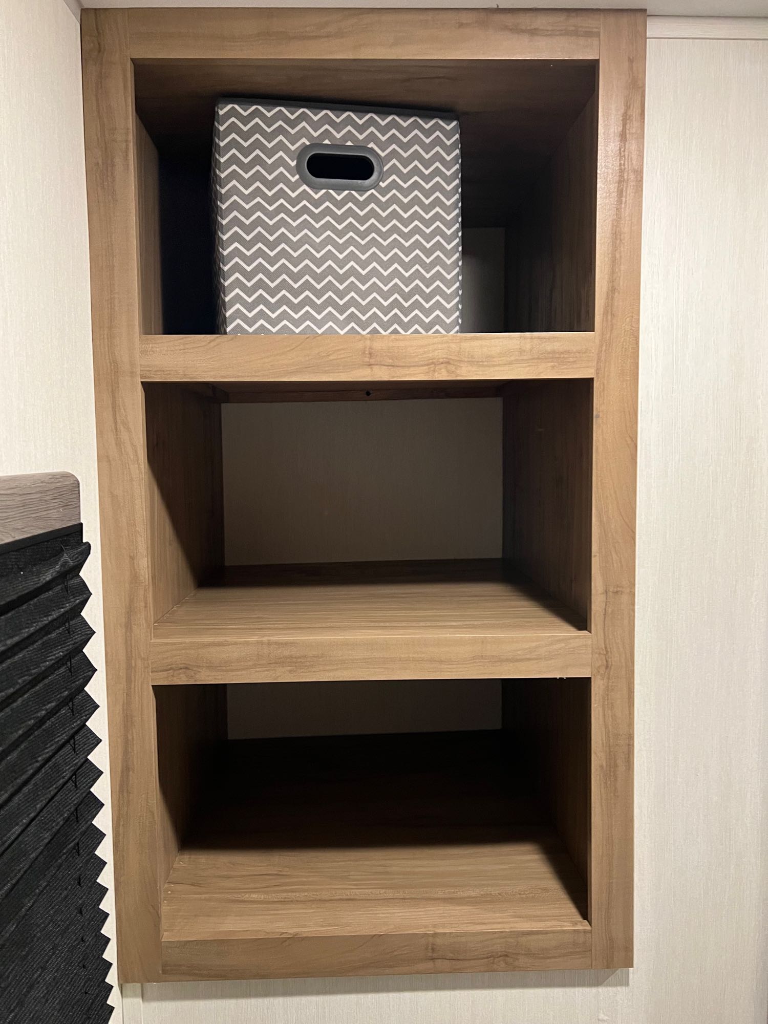 Practical RV rental storage: wooden built-in shelves, with a grey chevron storage bin on top, perfect for camper organization.. Forest River Campsite Reserve 2025