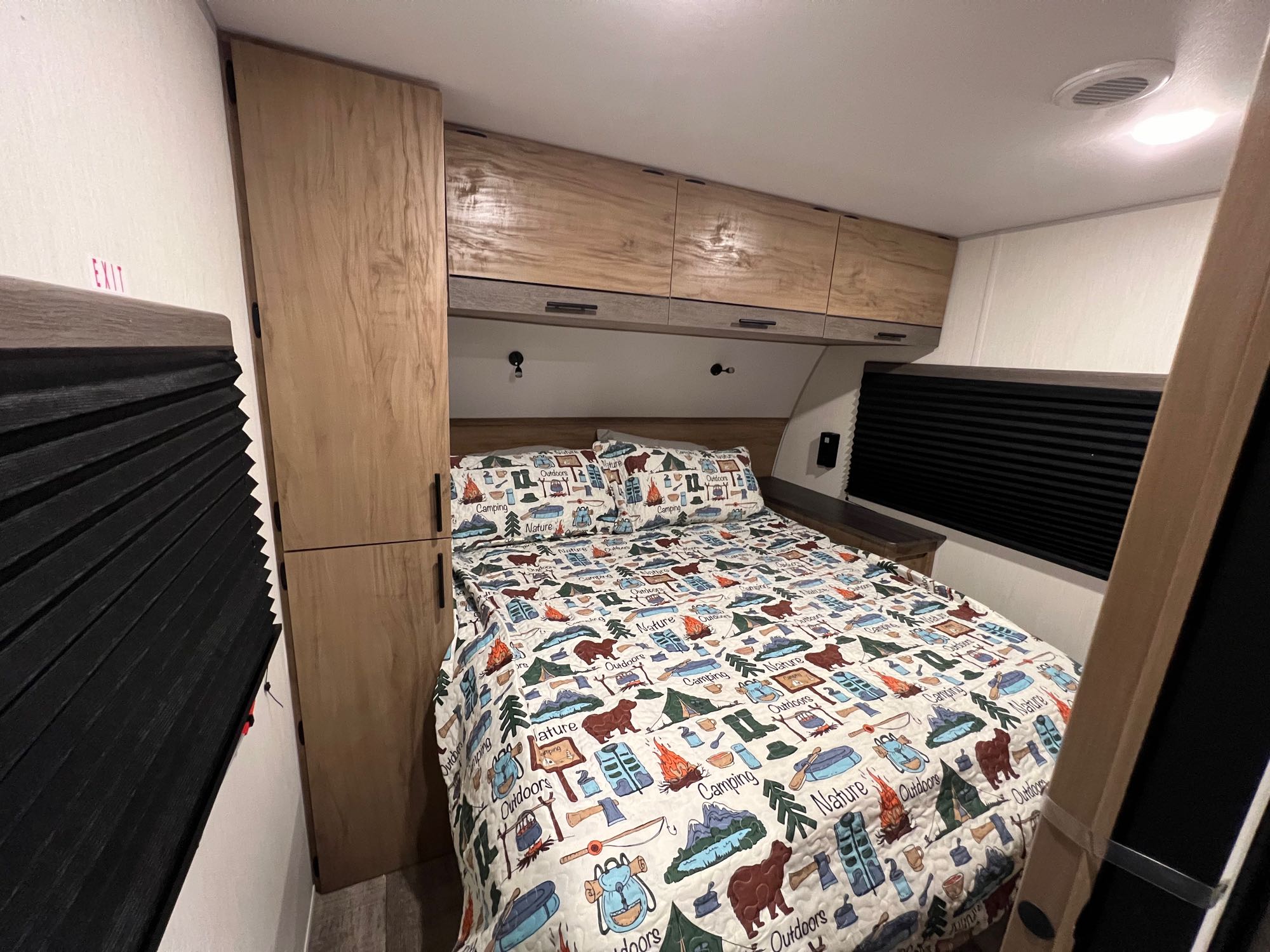 Cozy RV rental bedroom with camping-themed bedding, overhead cabinets, and built-in storage.. Forest River Campsite Reserve 2025