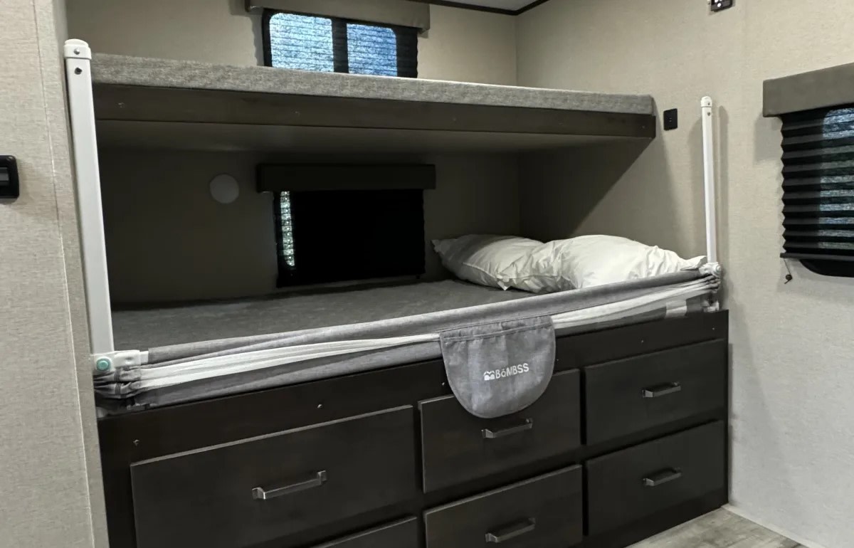 Comfortable RV rental interior with bunk beds, ideal for family travel. Features storage drawers and a safety rail for the lower bunk.. Grand Design Transcend Xplor 2023