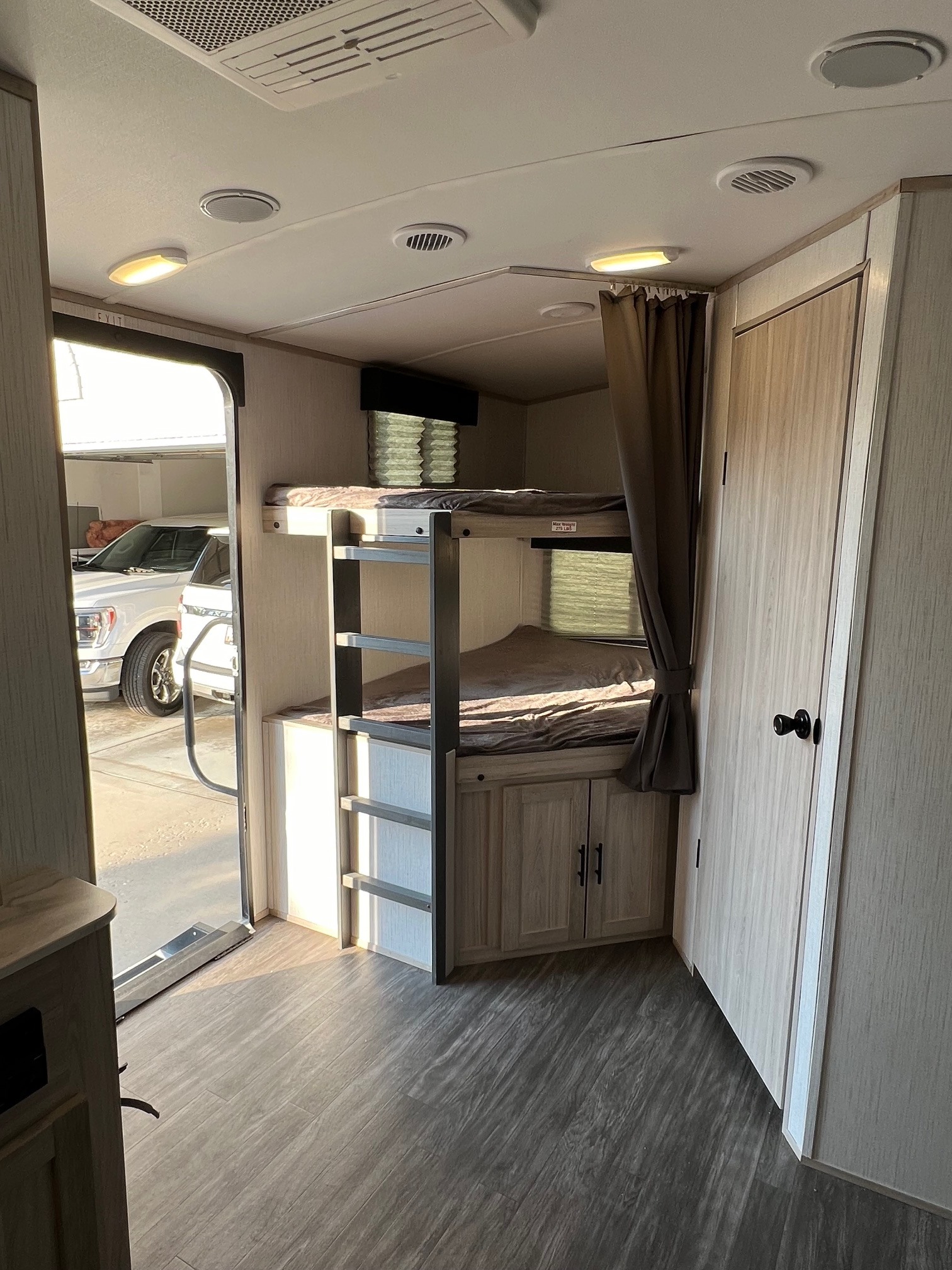 Inside an RV rental, featuring bunk beds, light wood-look flooring, and an open door showing a white truck outside.. Cruiser Rv Corp Shadow Cruiser 2022