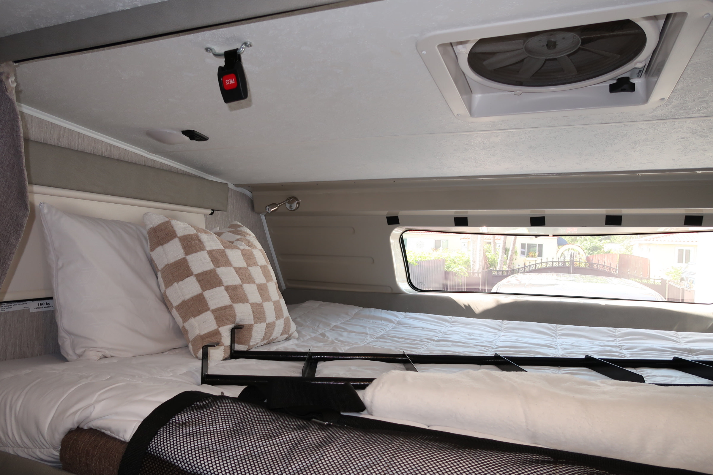 Cozy RV rental bed with a window view, ceiling fan, and safety buckle above.. Coachmen Leprechaun 2021