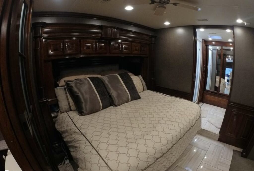 Luxurious RV rental bedroom features a spacious bed with patterned duvet, dark wood cabinetry, and a mirrored door.. American Coach Revolution 2017