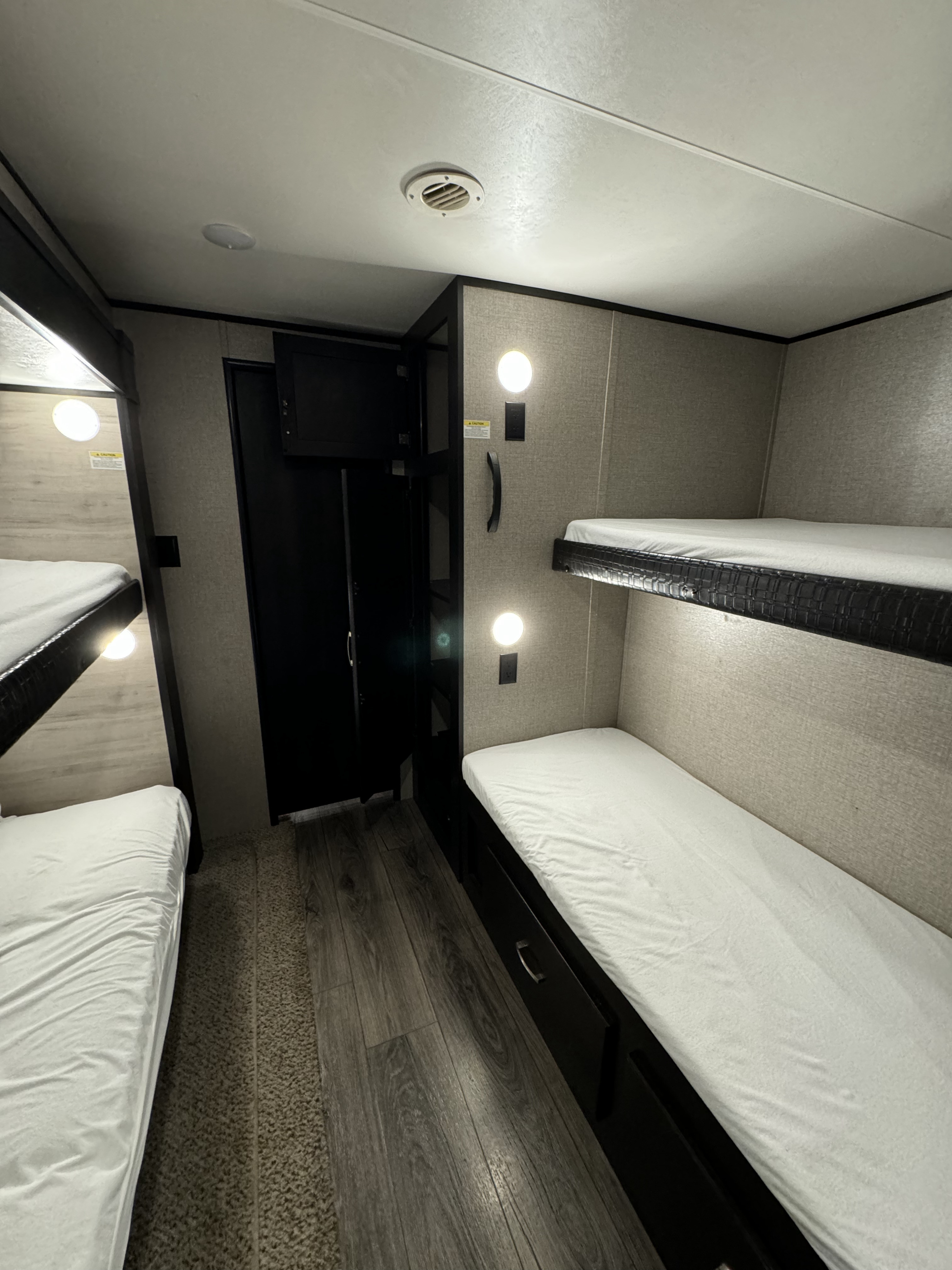 Compact RV rental bunk room featuring two sets of beds with white sheets, wall lights, storage, and mixed flooring.. Jayco Jay Flight 2021