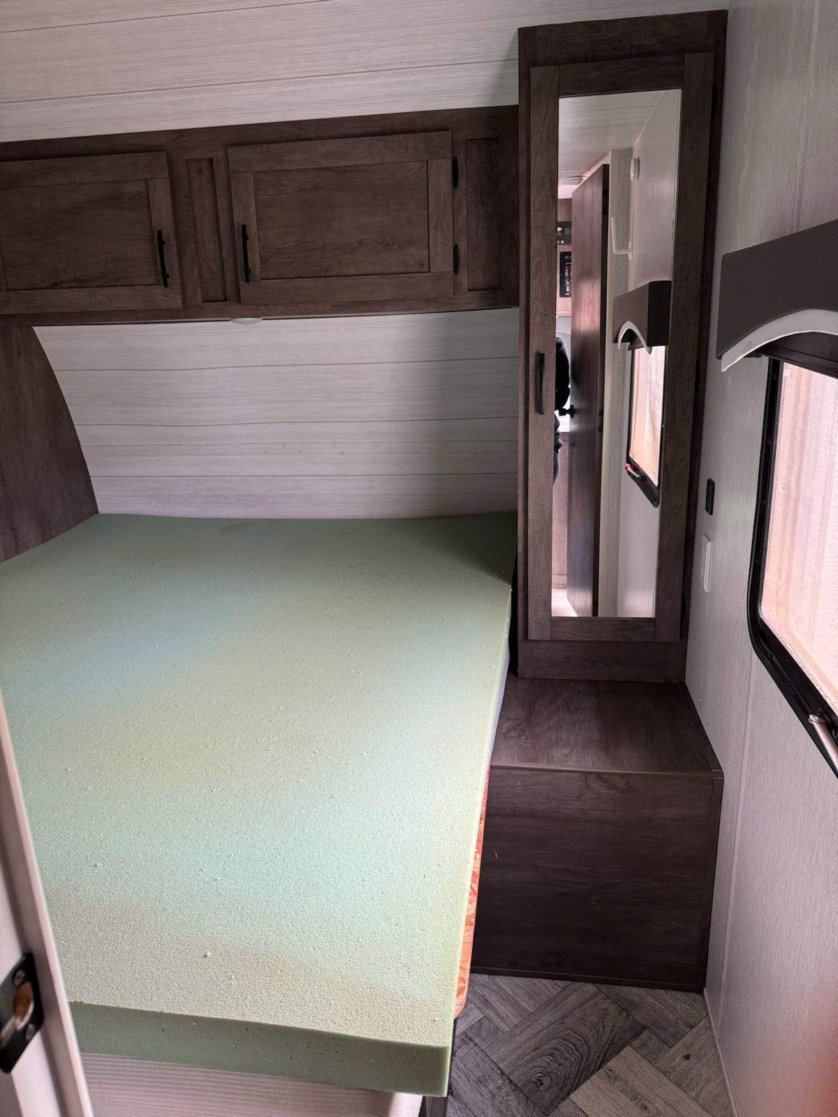 RV rental bedroom with light green foam mattress, dark wood overhead cabinets, and a full-length mirror.. Forest River EVO 2022