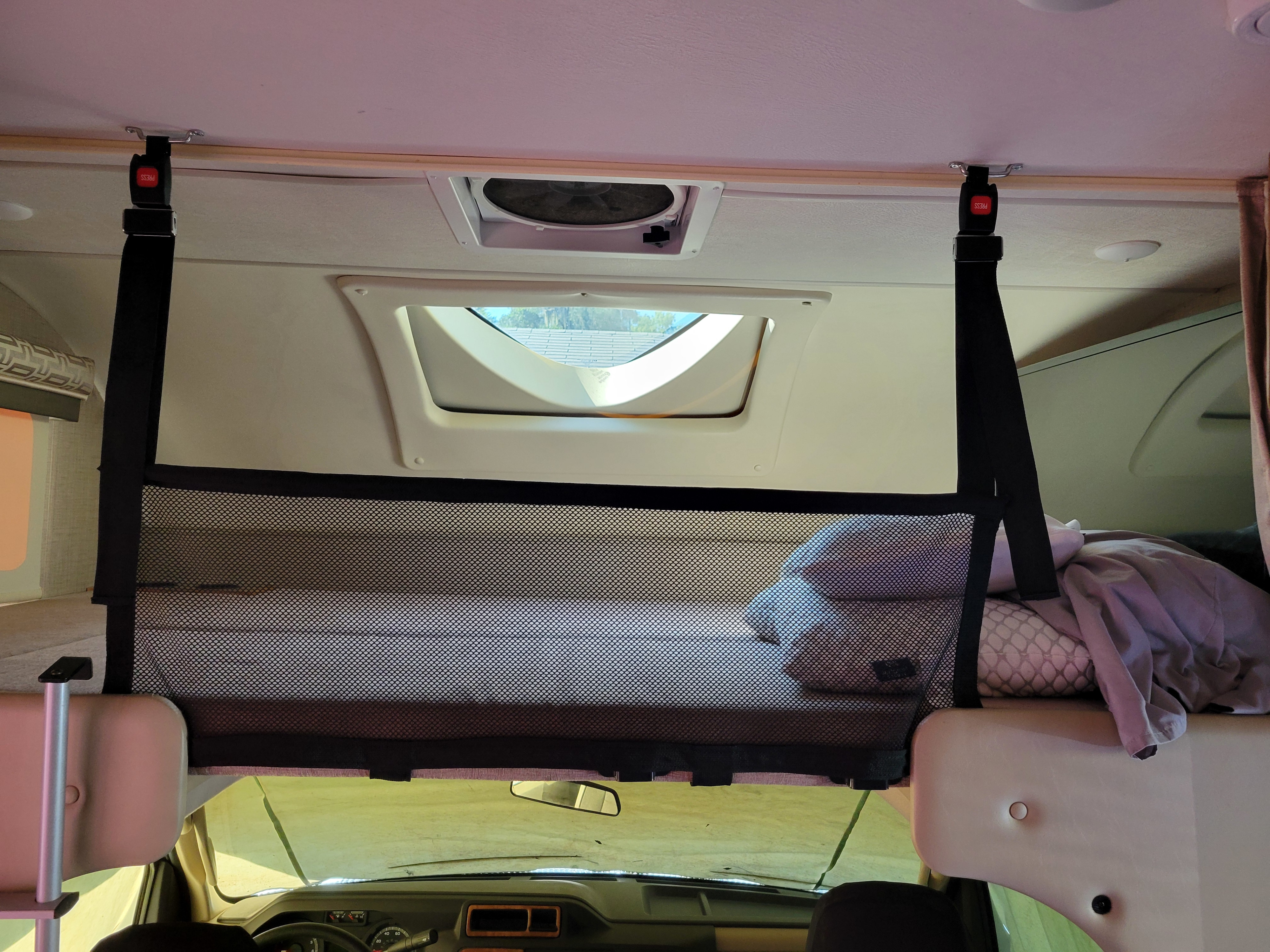 Overhead bunk area in an RV rental, featuring a safety net, skylight, and cozy bedding. Vehicle dashboard is visible below.. Thor Quantum 2018