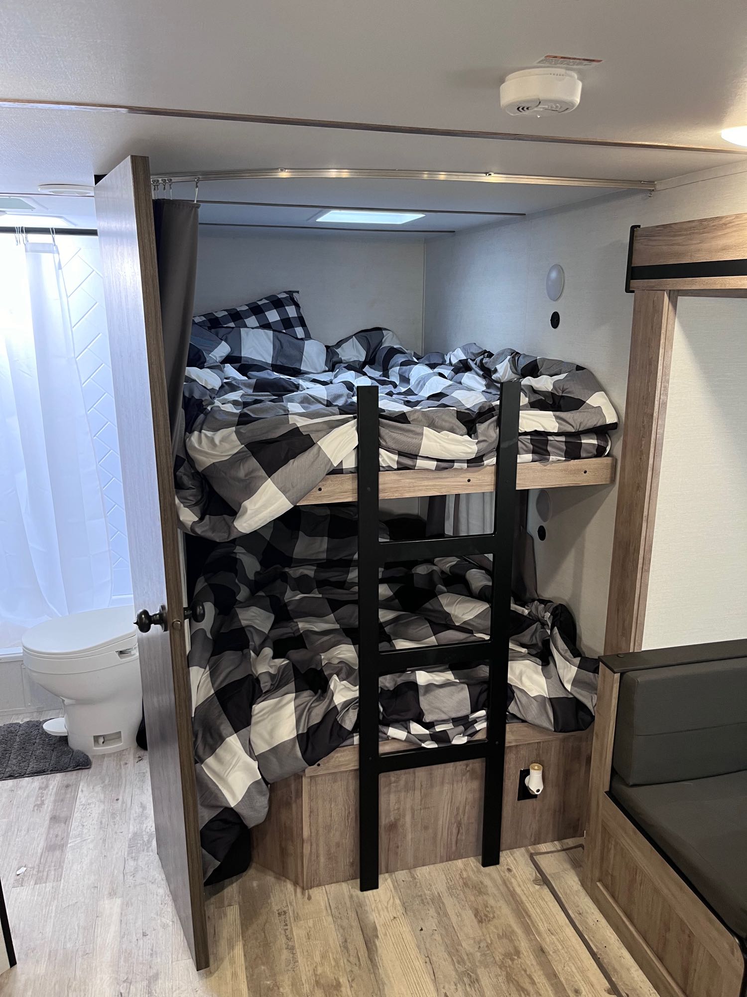 Cozy RV rental interior featuring comfortable bunk beds with plaid bedding, a nearby compact bathroom, and seating.. Grand river 27BHS 2024