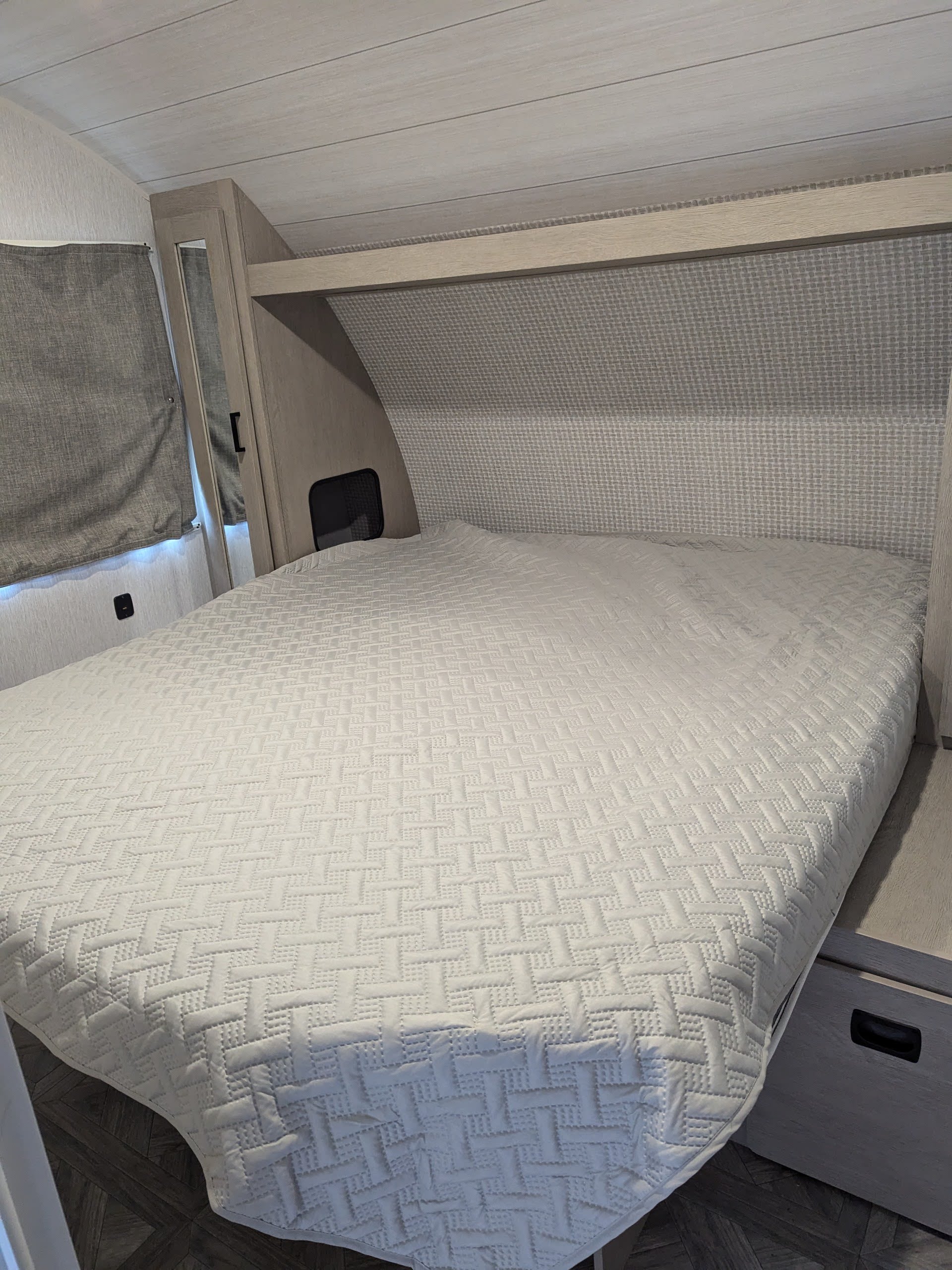 RV rental bedroom with a comfy white quilted bed, built-in storage, and window. A cozy space.. Forest River Wildwood X-Lite Platinum 2024
