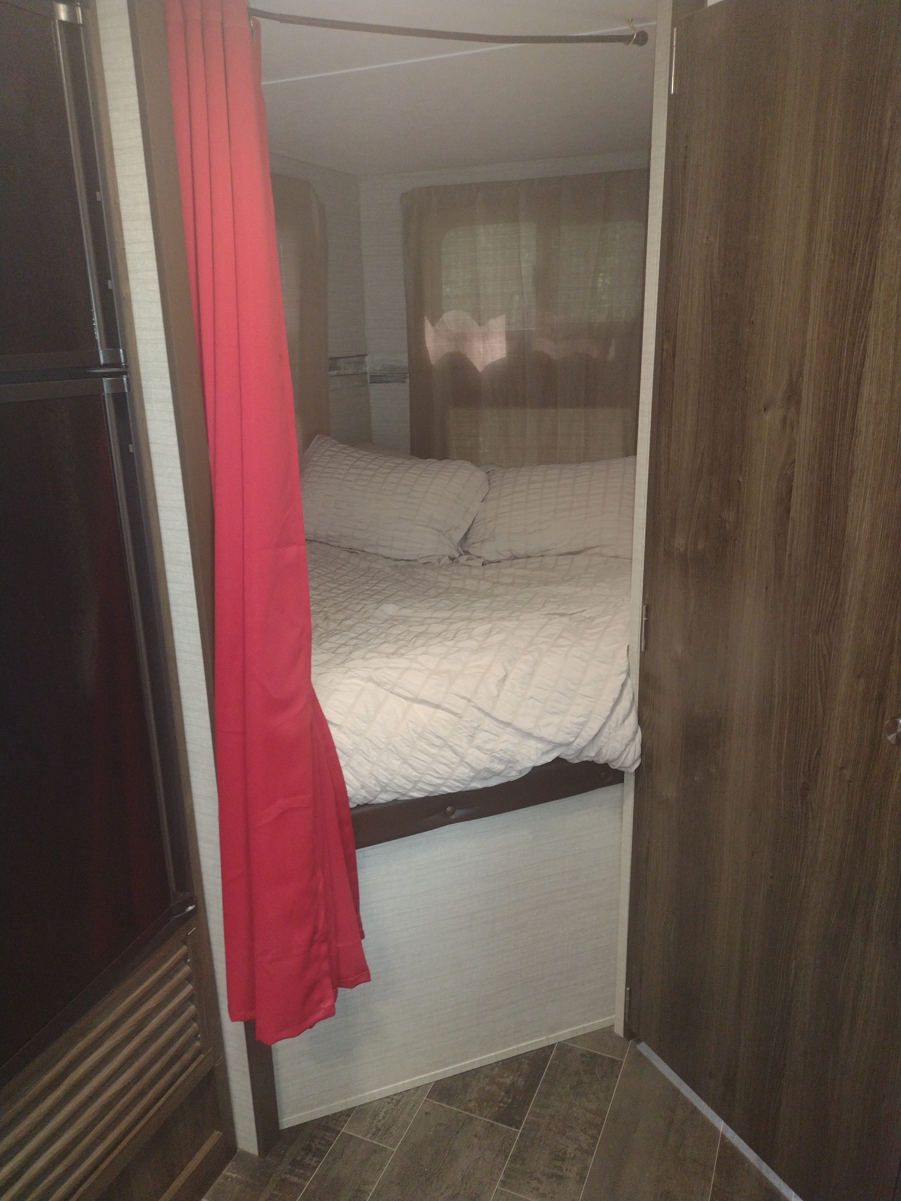 This rv rental showcases a compact, cozy bedroom with white bedding, pillows, and a vibrant red curtain for privacy.. Keystone RV Bullet Ultra Lite 2018