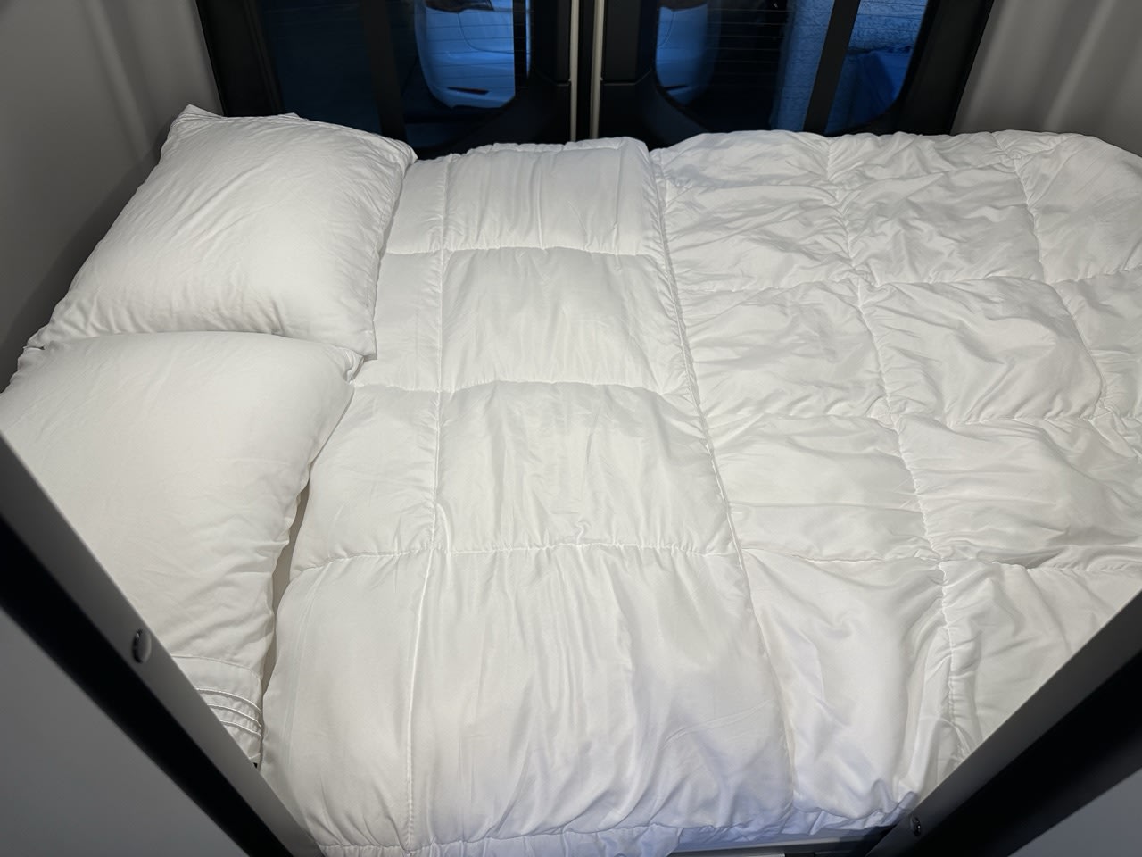 Neatly made white bed with pillows & quilted comforter in an rv rental, ready for a cozy night.. Winnebago Revel 2023