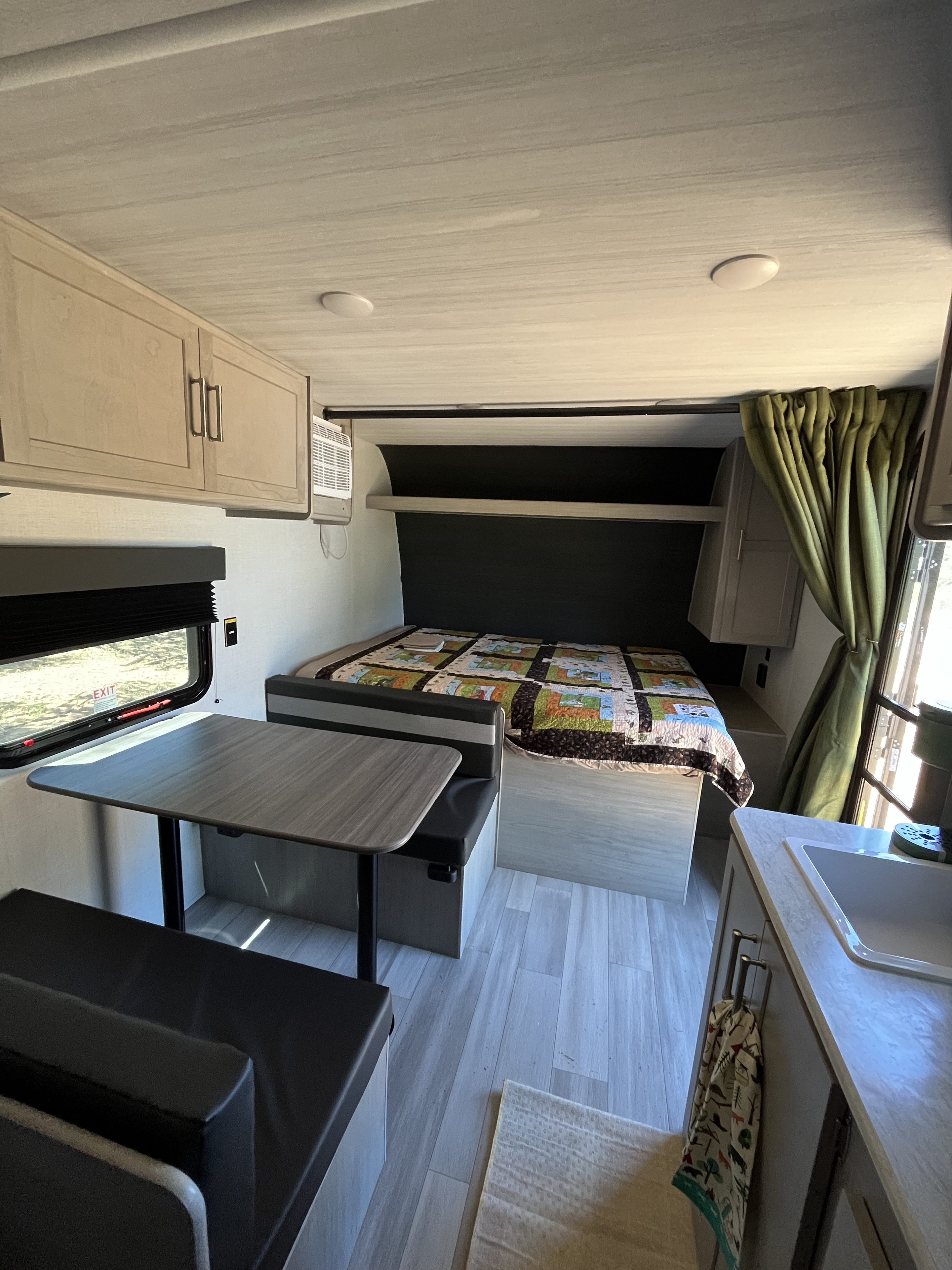 Inside this RV rental: a cozy interior with a dining area, bed, and compact kitchen sink, featuring light wood finishes.. Keystone RV Springdale 2024
