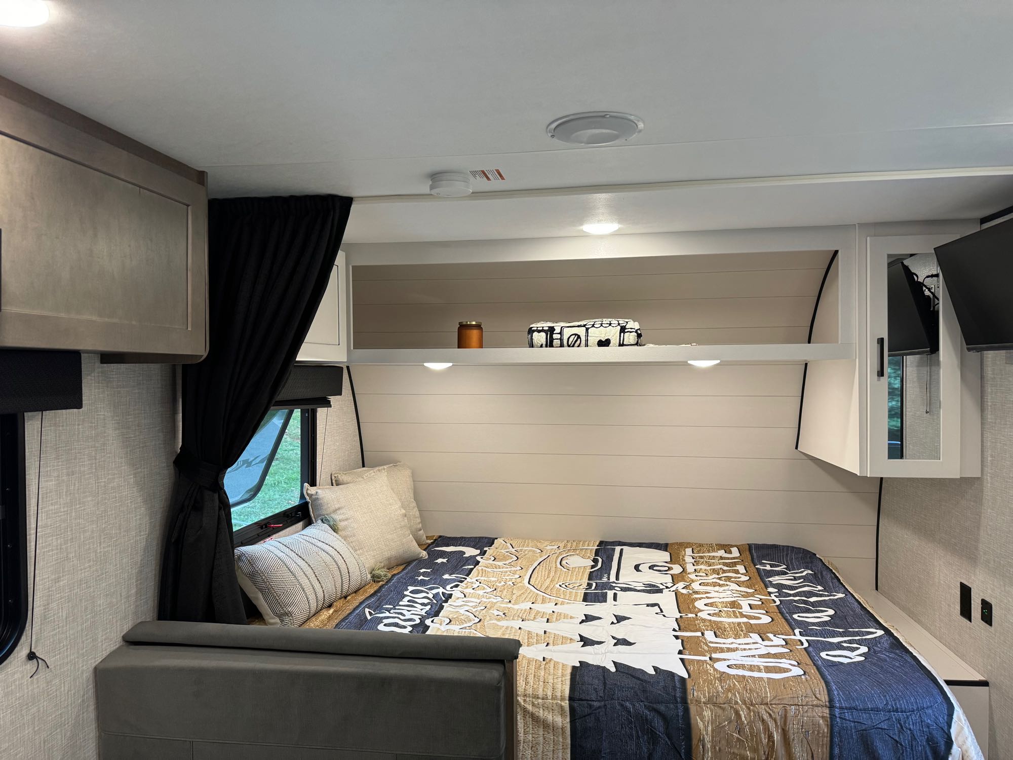 Inside a comfortable RV rental bedroom featuring a full bed, decorative pillows, storage cabinets, and a window with curtains.. Jayco Free Flight SLX 2025