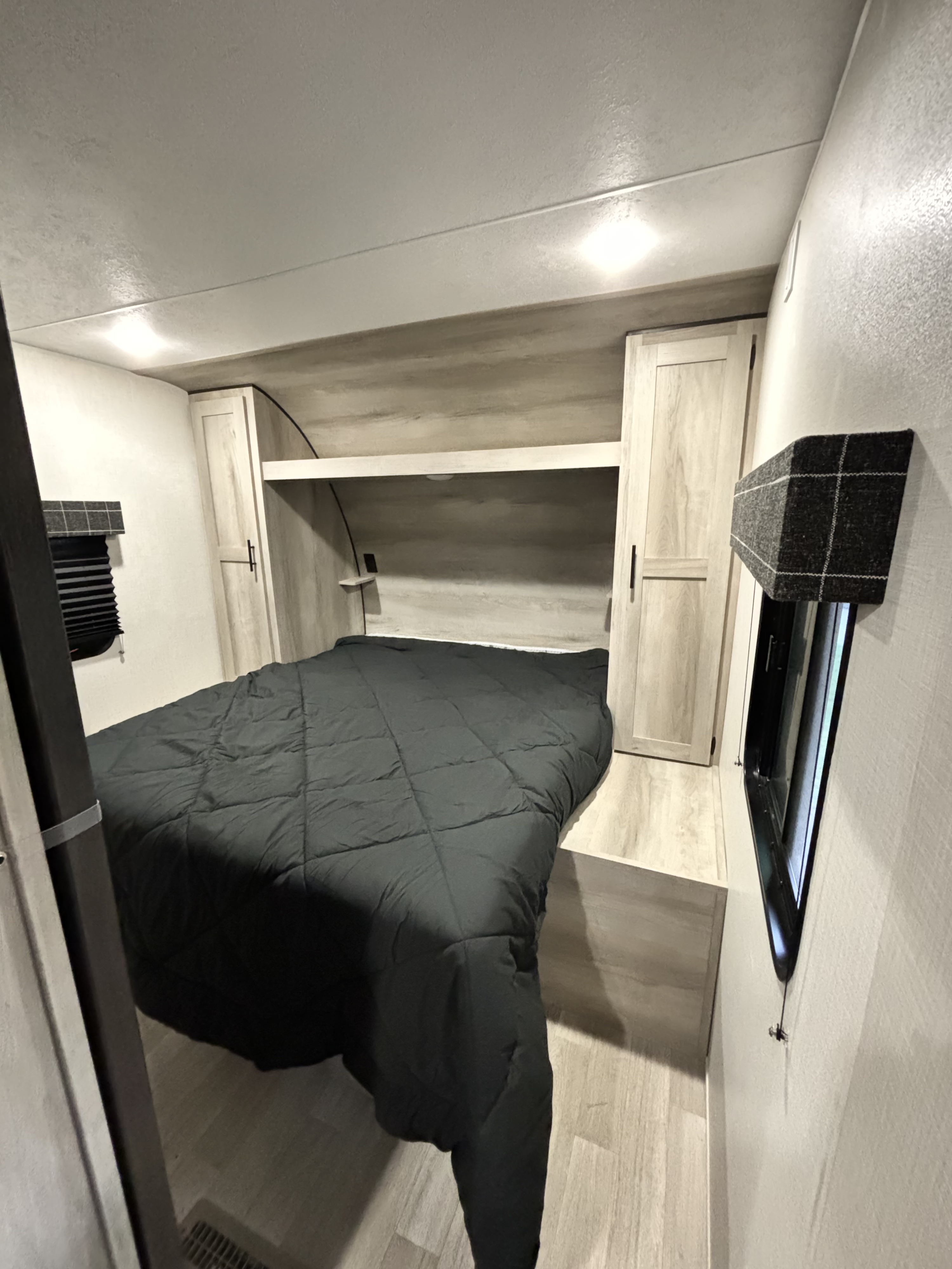 Cozy RV rental bedroom interior features a dark bed, light wood built-in cabinets, and practical window coverings.. Sportsmen 261BHKSE 2024