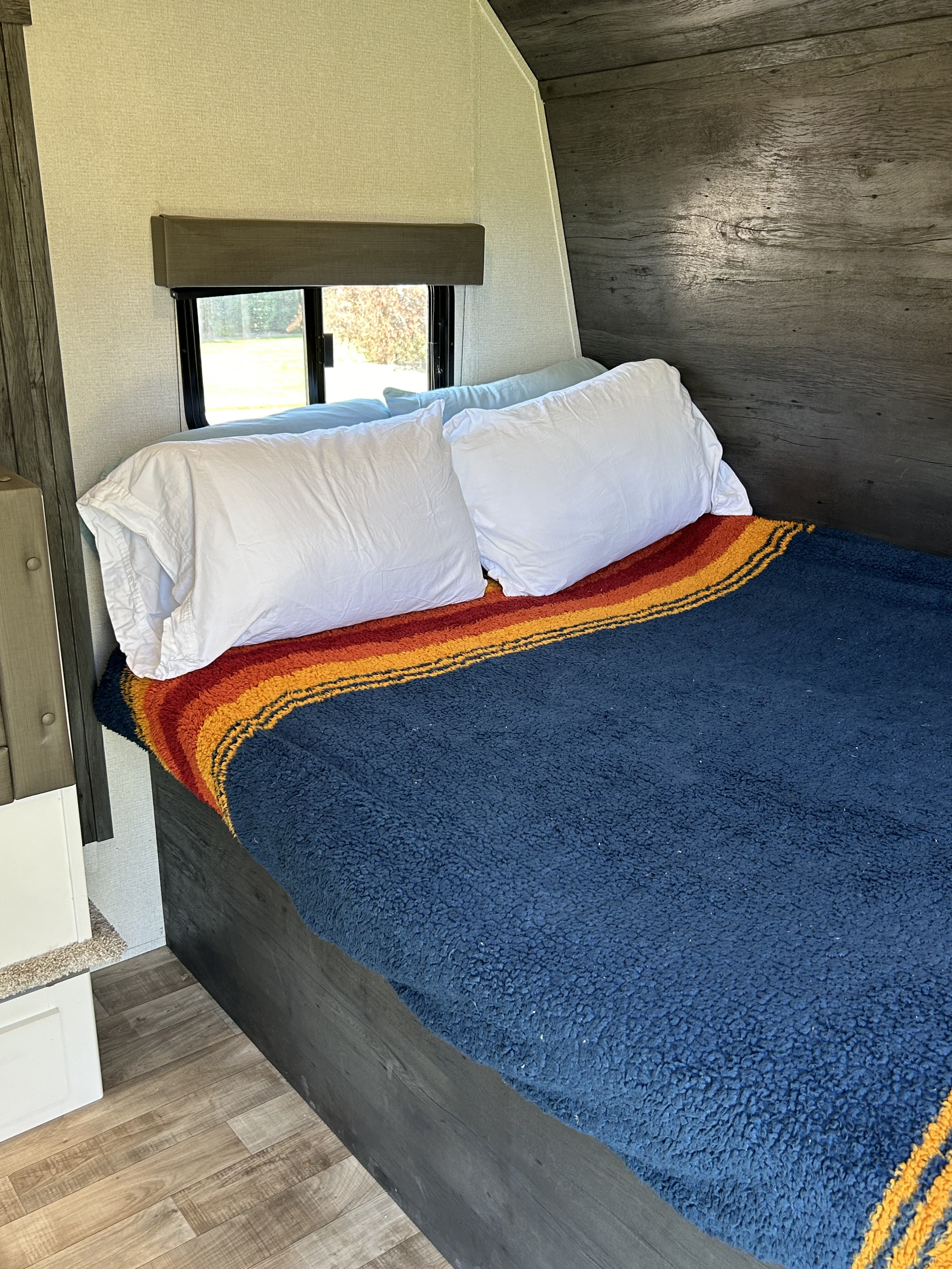 Cozy RV rental bedroom with striped blanket, white pillows, wood accents, and window view.. Keystone RV Hideout 2022