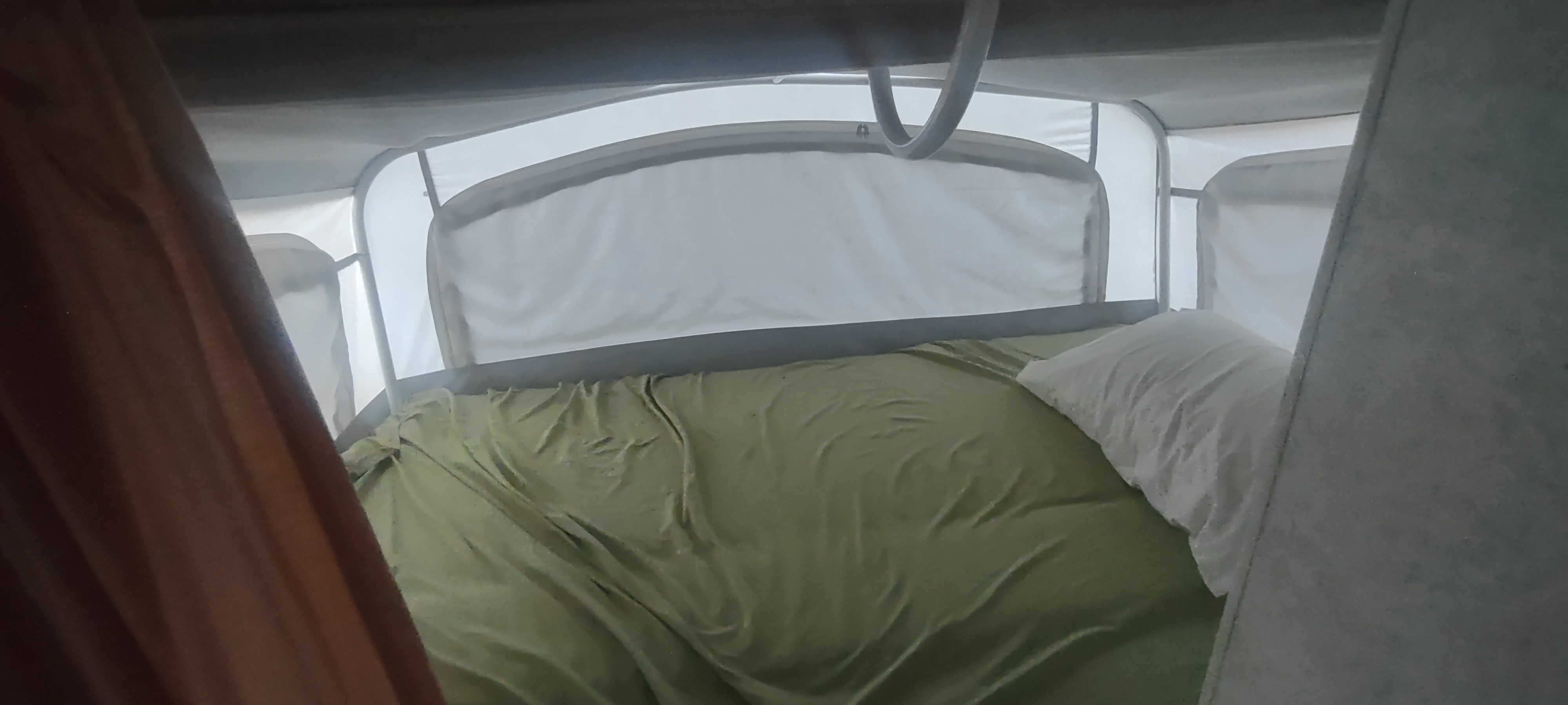 An RV rental pop-up camper's sleeping area: a bed with olive green sheets and a white pillow, ready for comfort.. Fleetwood Prowler ultra lite 2000