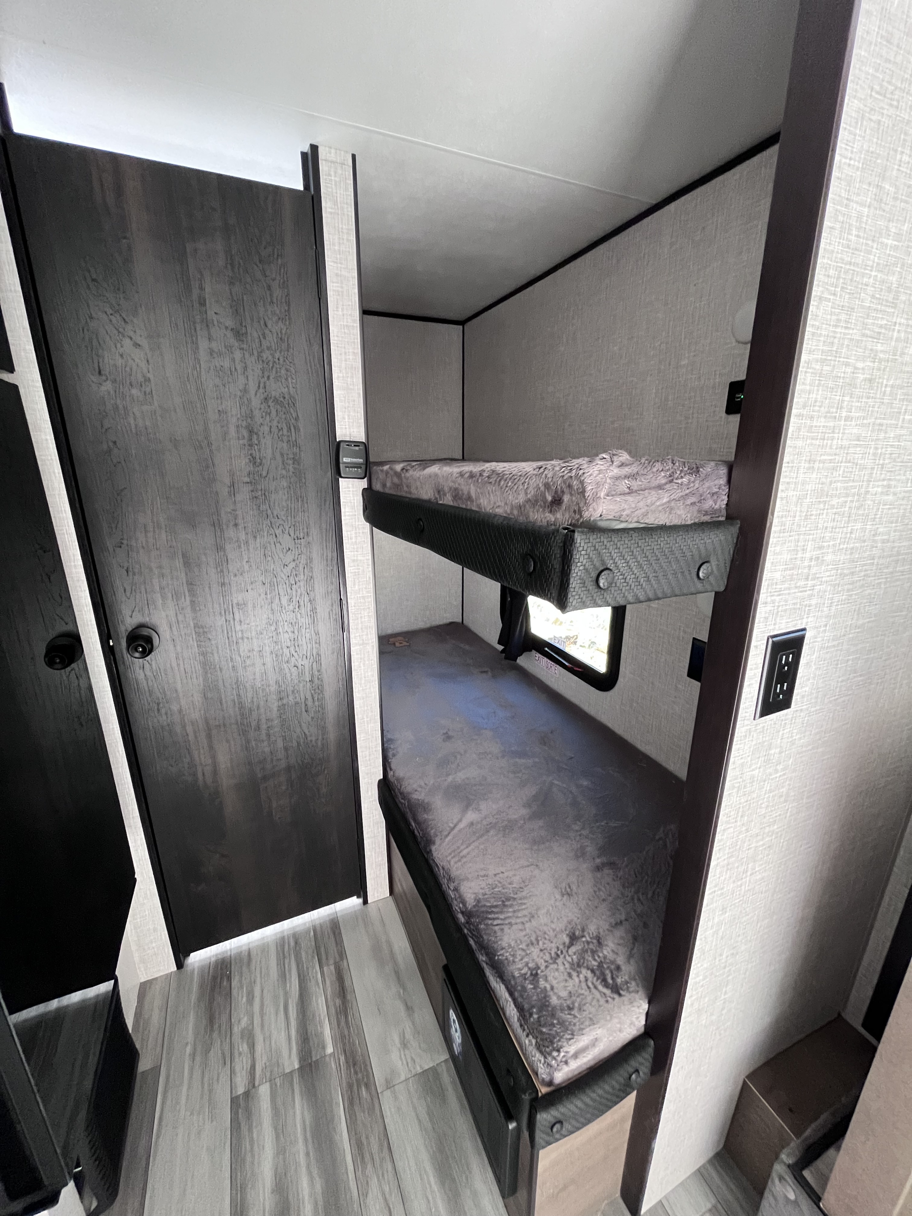 RV rental interior features cozy bunk beds with fuzzy covers, a dark wood door, and light wood-look flooring.. JAYCO Flight SLX 184BSW BAJA 2024
