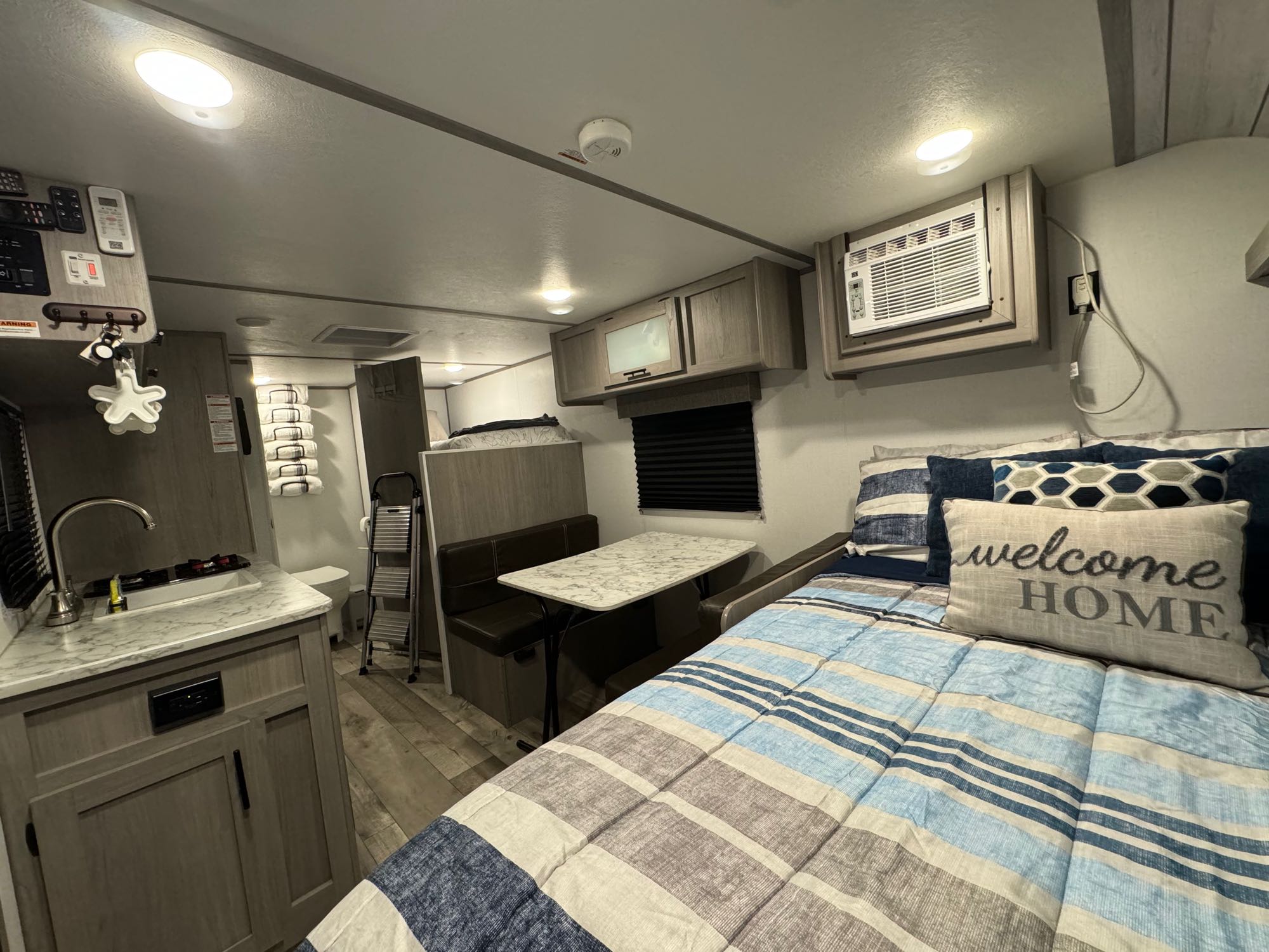 Discover this cozy RV rental interior, featuring a kitchen, dining booth, and comfortable bed with a 'Welcome HOME' pillow.. Coleman Lantern LT 17B 2024