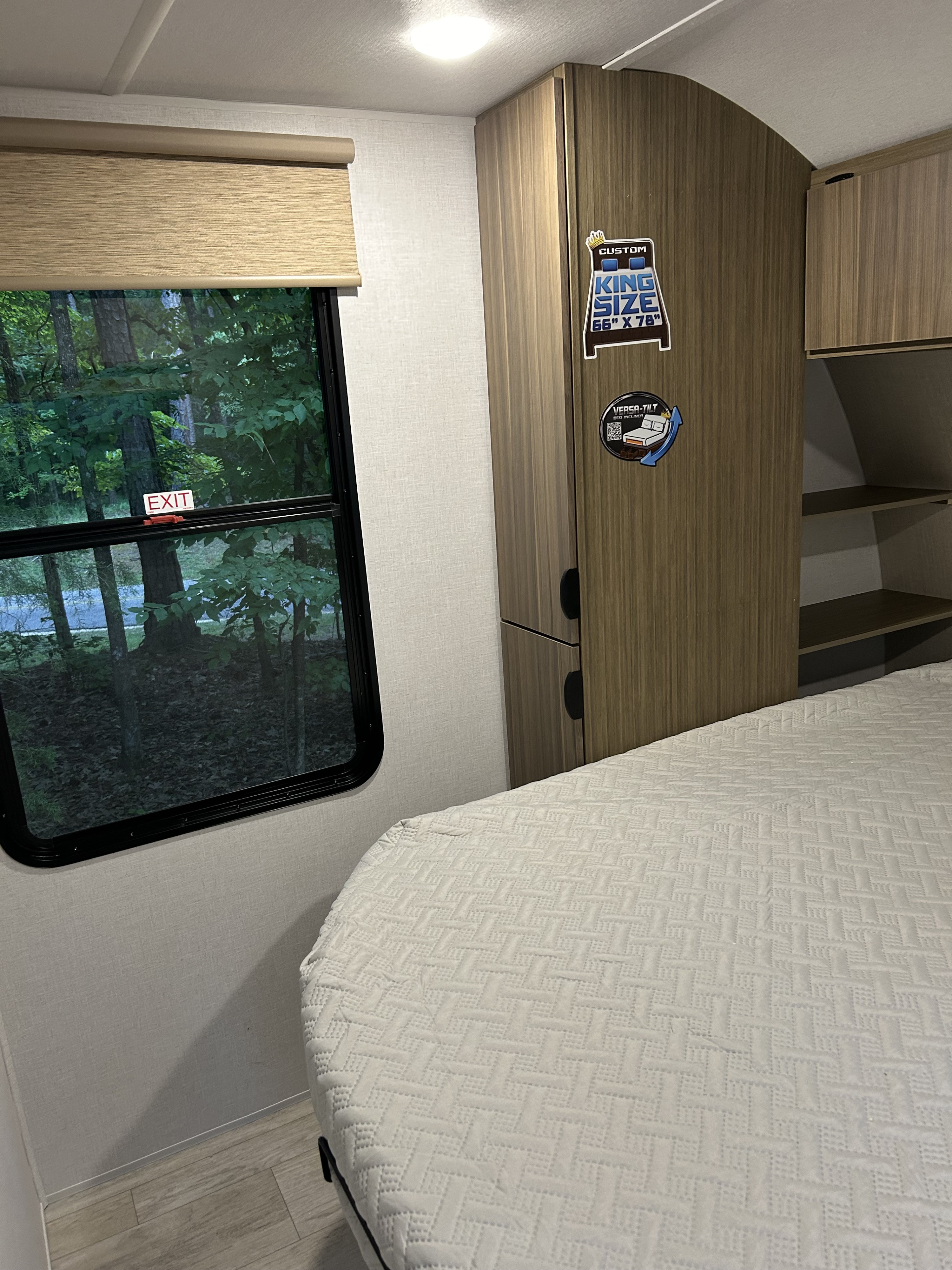 Explore this cozy RV rental bedroom featuring a custom king bed, window with nature views, and built-in storage cabinets.. Forest River RV Wildwood 31KQBTSX 2025