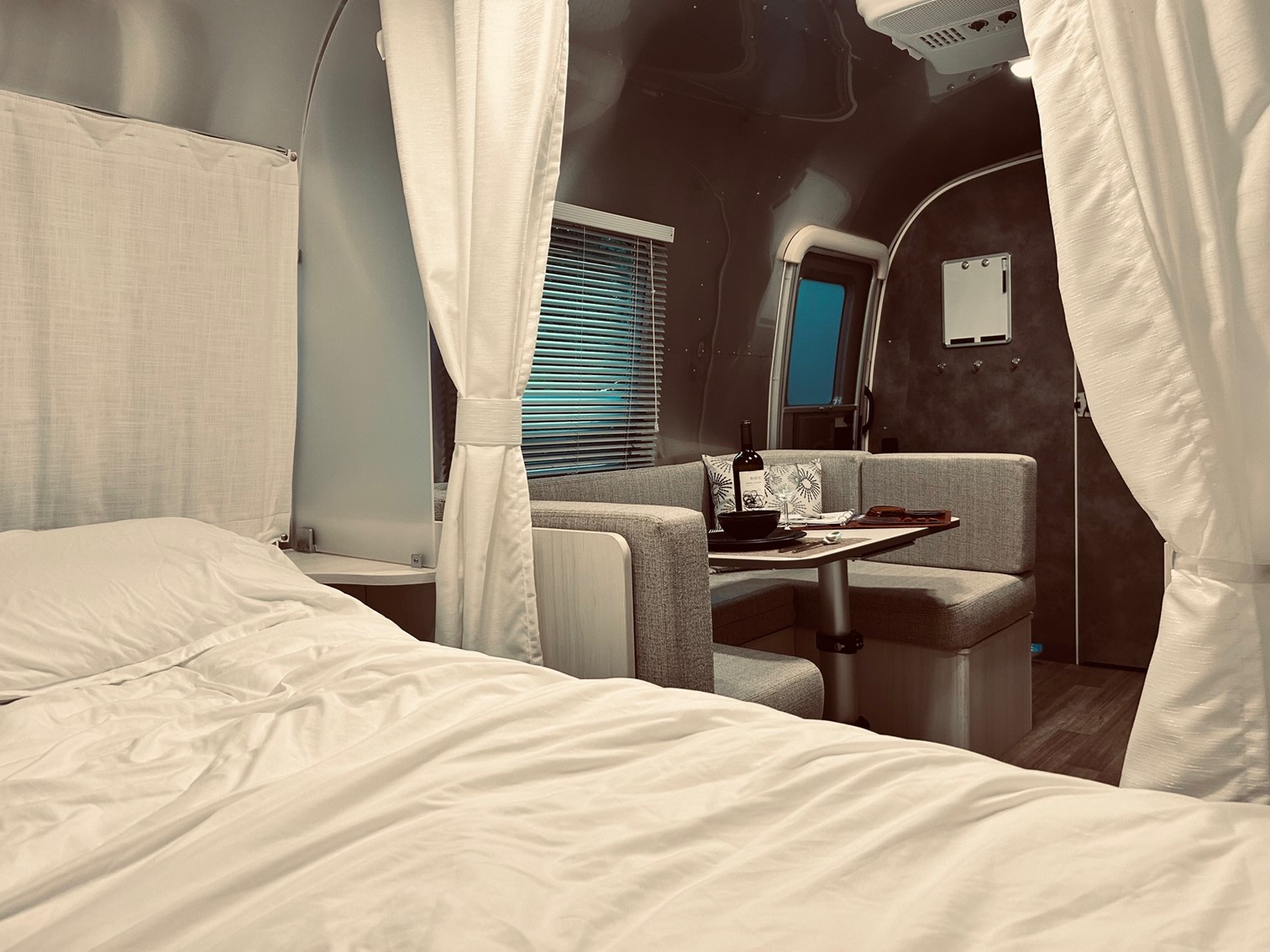 Experience comfortable RV rental travel! This Airstream interior features a cozy bed in the foreground and a dining area.. Airstream Bambi 2022