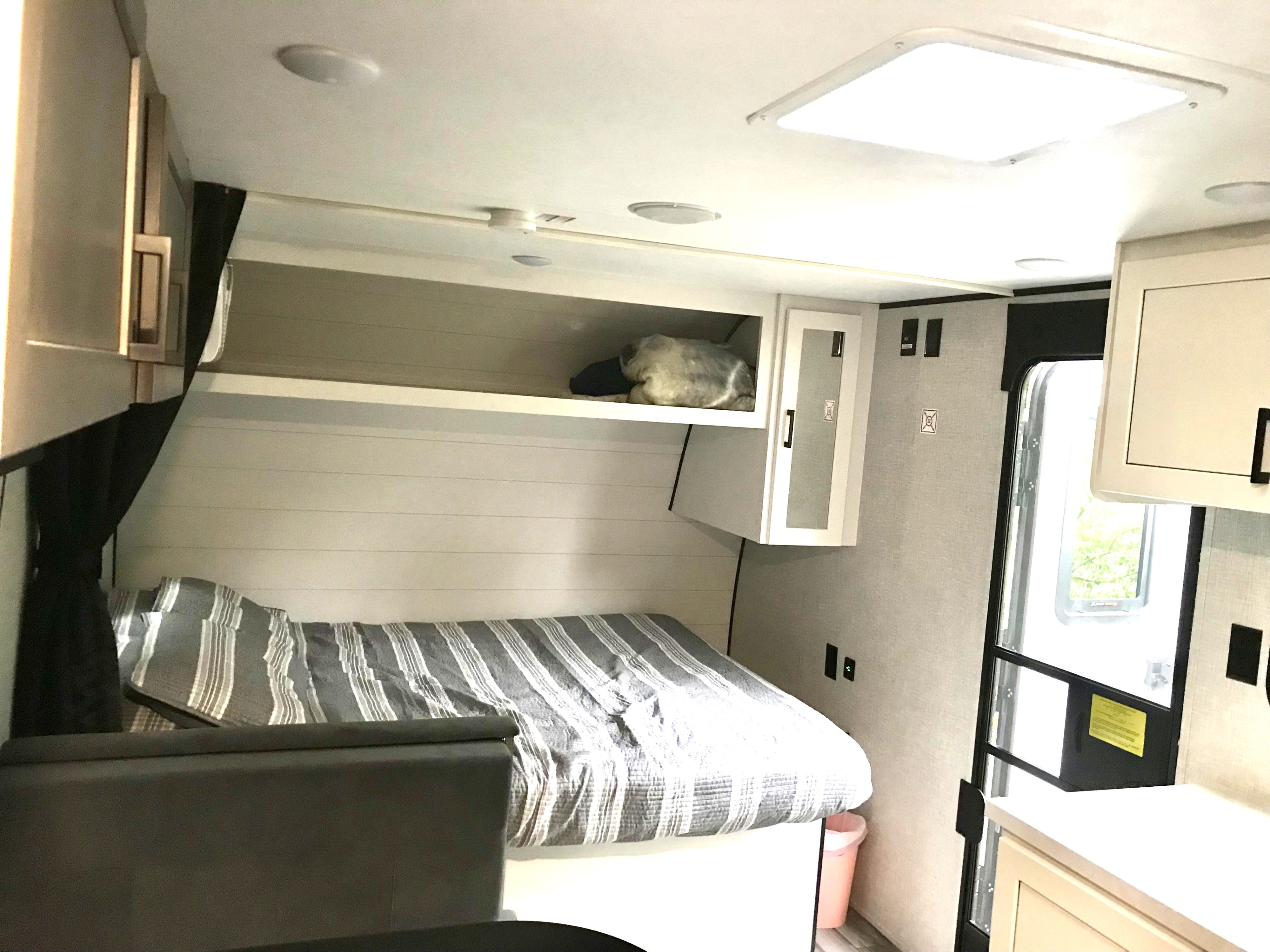 RV rental interior: cozy raised bed with striped bedding, overhead storage, and light-colored walls and cabinets.. Jayco SLX 2025