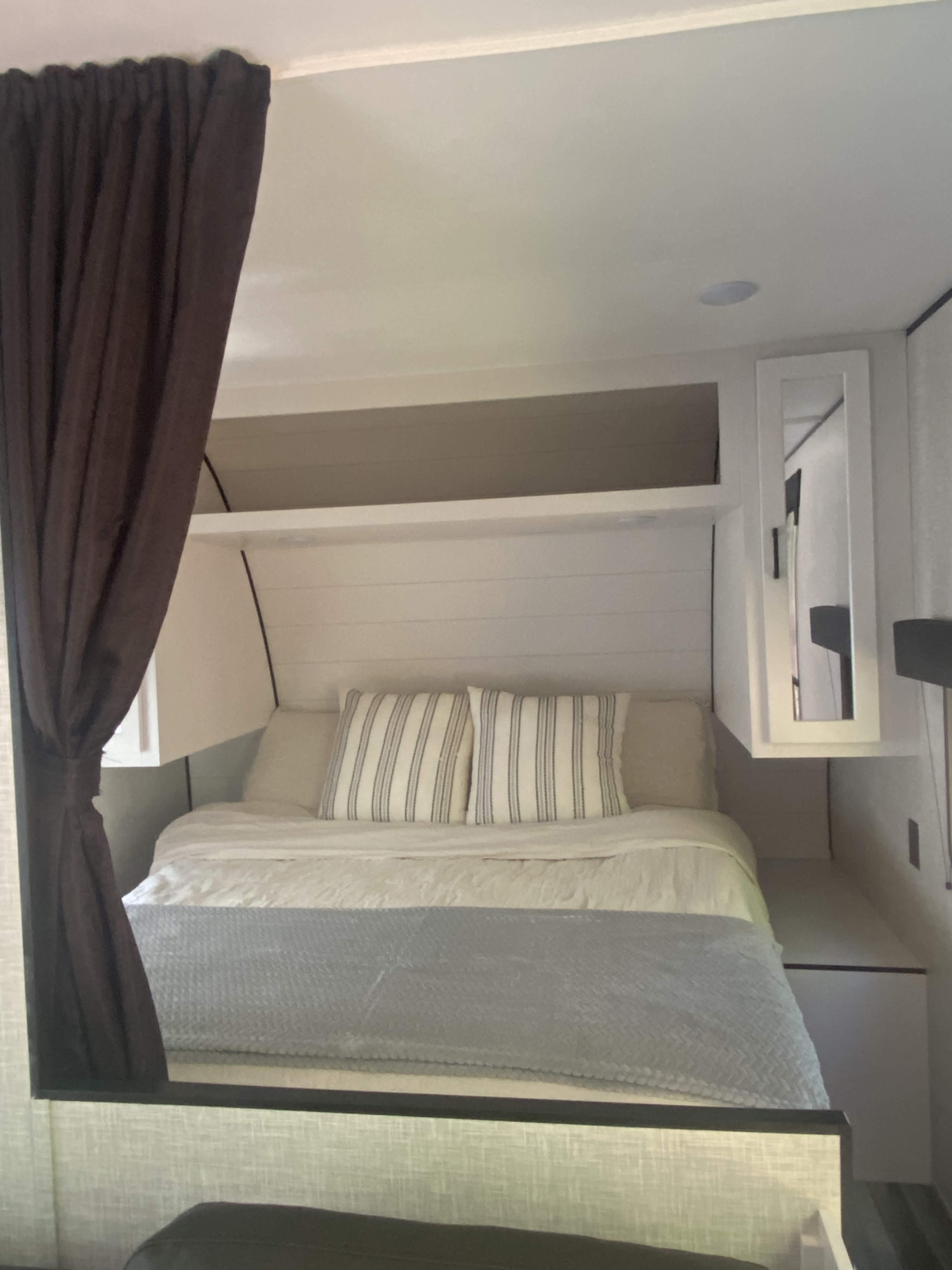 Clean and cozy RV rental bedroom features a comfy bed with striped pillows, dark curtains, and overhead storage.. Jayco Jay Flight SLX 2024